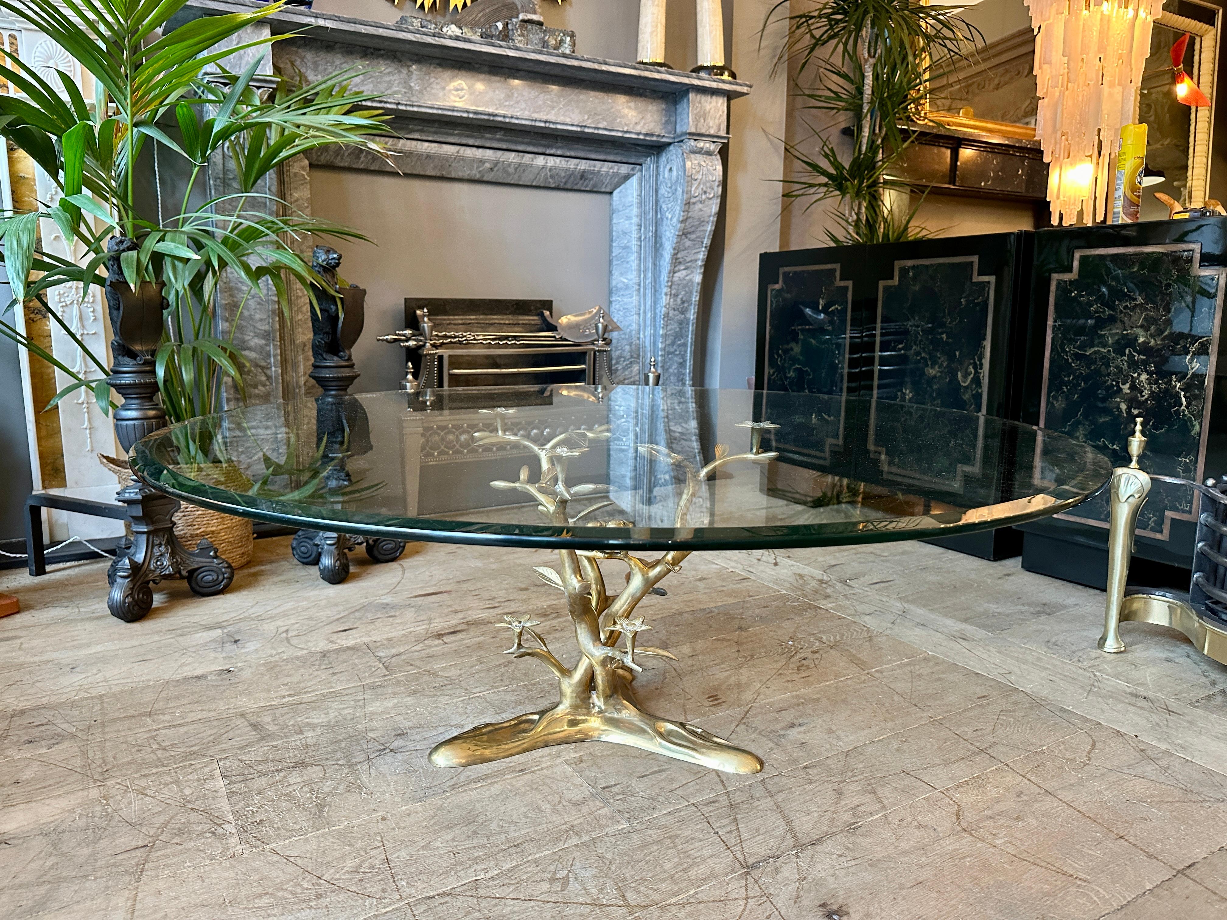 A large glass circular topped coffee or cocktail table with cast brass base of a tree with tropical birds perched within. The circular top with bevelled edge, some light wear to top. The base very well cast with tripod organic feet. All in good