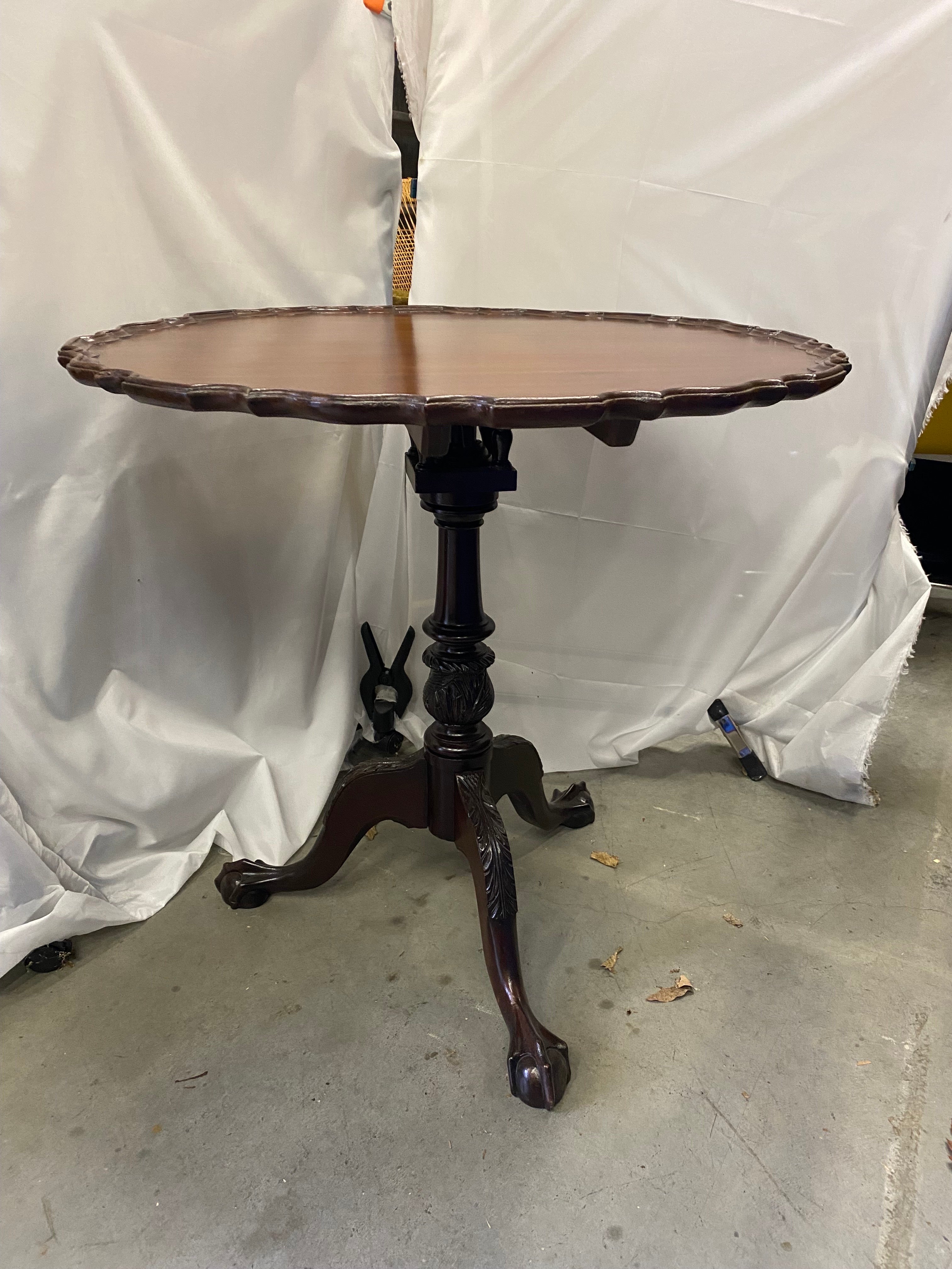 A classic hand carved Centennial Chippendale tilt top piecrust tea table. The shaped circular top with birdcage beneath, the ring turned and carved central support, raised on a tripod base with acanthus carved knees to the cabriole legs, terminating