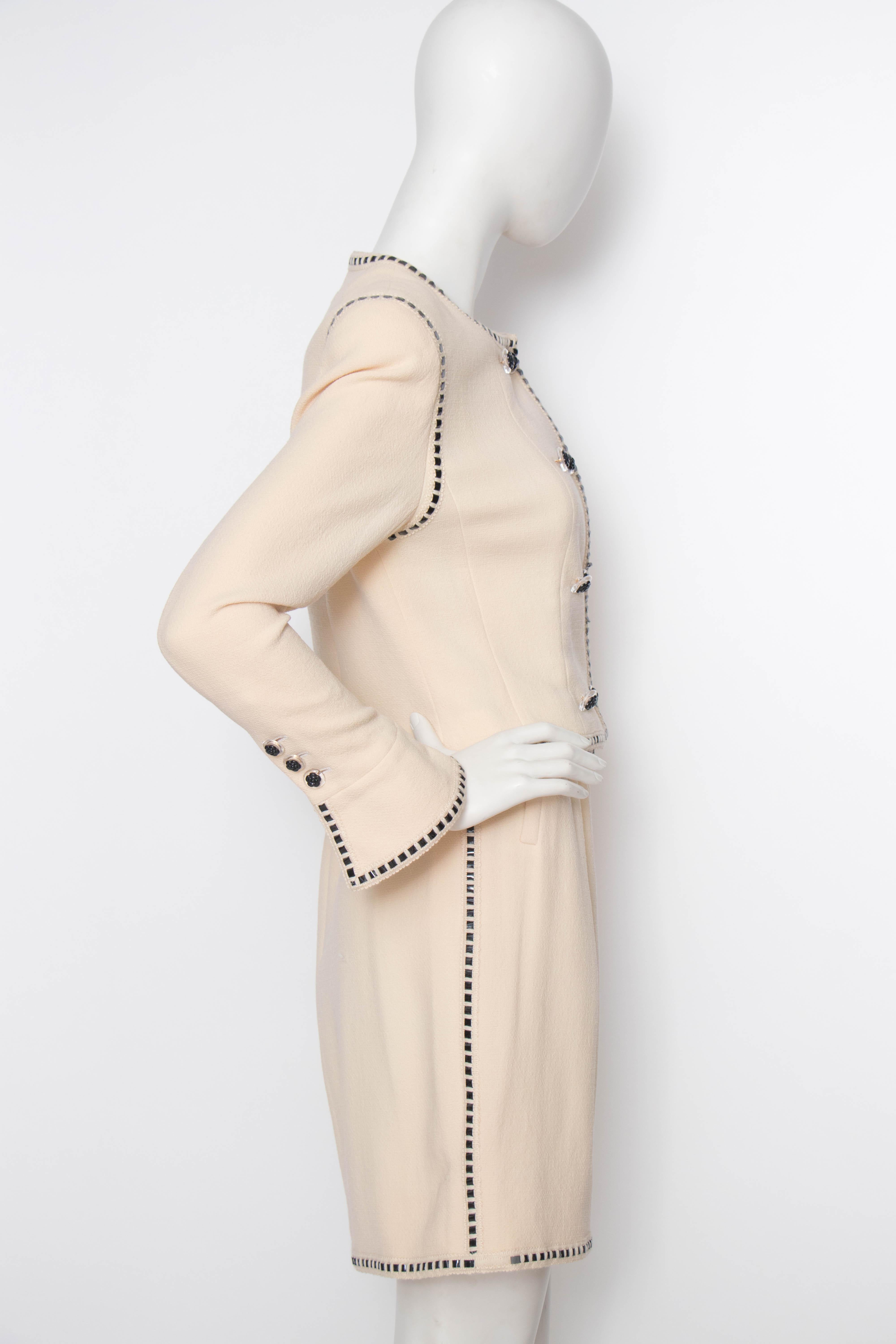 A classic ivory Chanel skirt suit consisting of a fitted pencil skirt and cropped jacket. The jacket has a double-breasted closure and incredibly detailed cuffs. Both the skirt and jacket have black PVC trim. The Chanel buttons consist of a clear