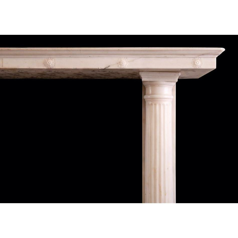 Ein eleganter Regency-Kamin aus weißem Statuary-Marmor. Die Türpfosten mit klassischen, kannelierten Säulen an der Vorderseite und halbrunden Säulen an der Rückseite. Das Regal ist mit Rosetten und einer zentralen Tafel mit Glockenblumen und Schalen