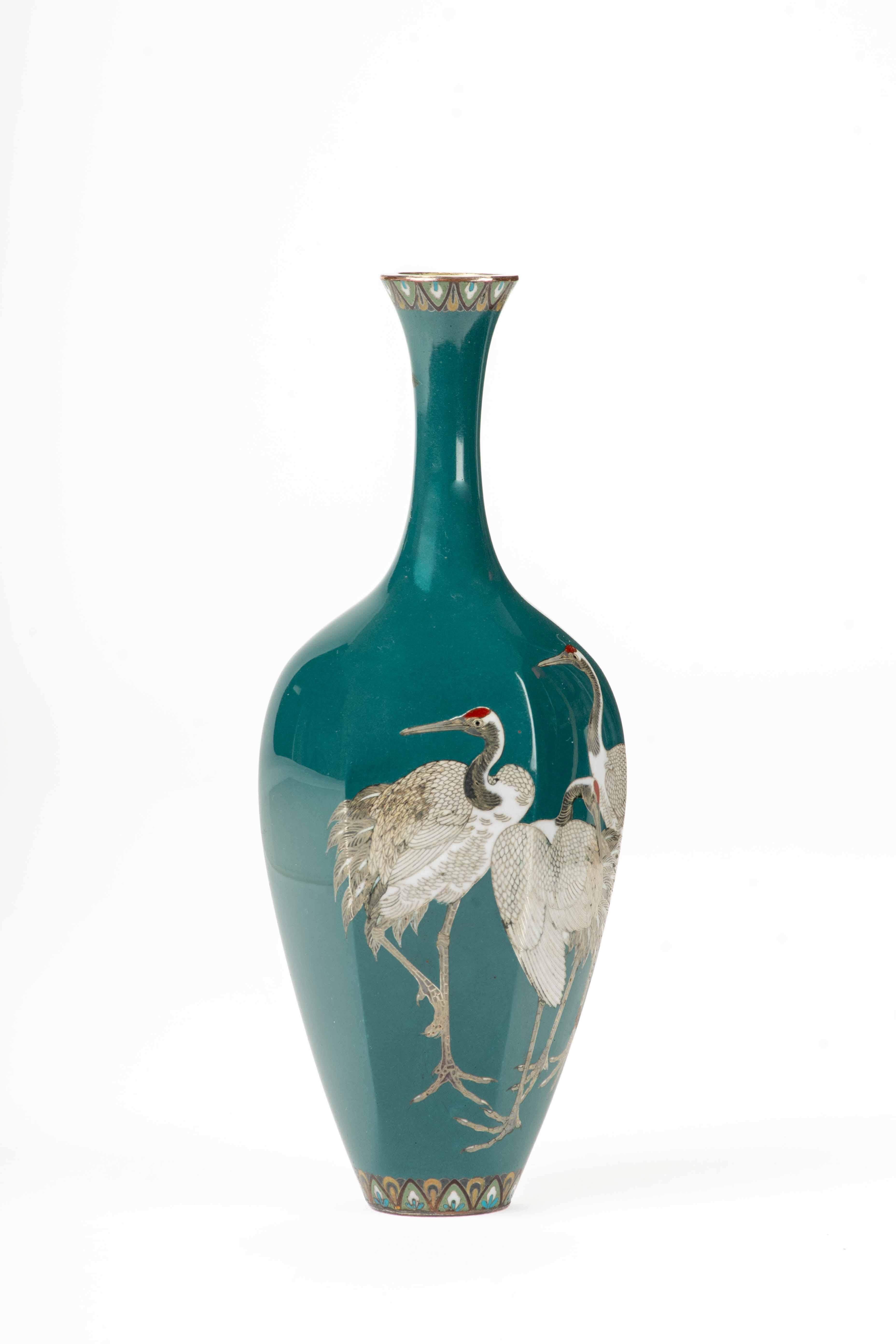 A hexagonal cloisonné vase with an elongated neck, depicting three Manchurian cranes with plumage rendered in polychrome enamels on a turquoise ground.

The enamels are defined by fine silver wires that enhance the contours and add