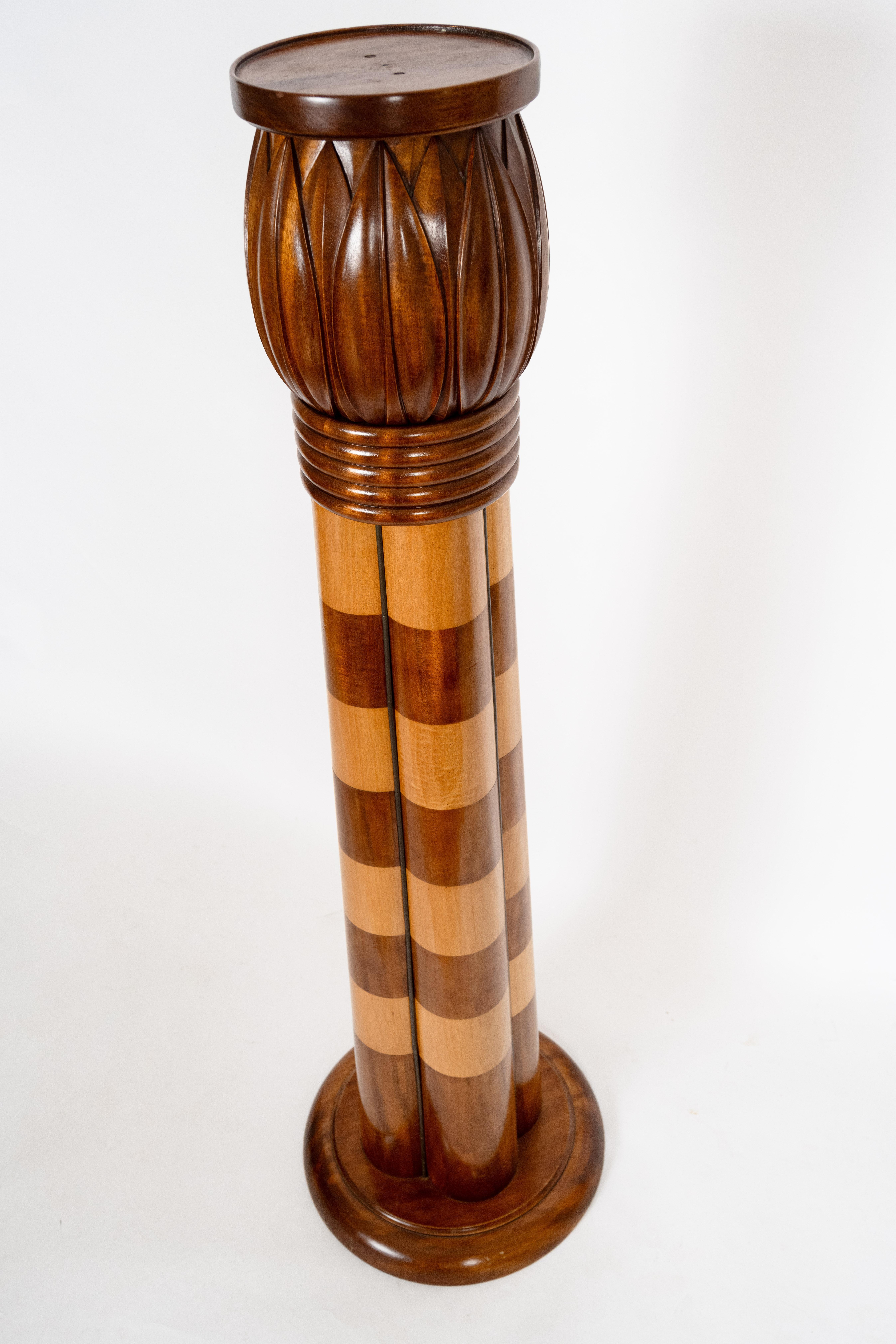 A cluster column form pedestal. The tapered base supported by a round plinth and having a stylized lotus flower carved element at the top. The base in contrasting light and medium colored satin wood  in walnut. Circa 1900