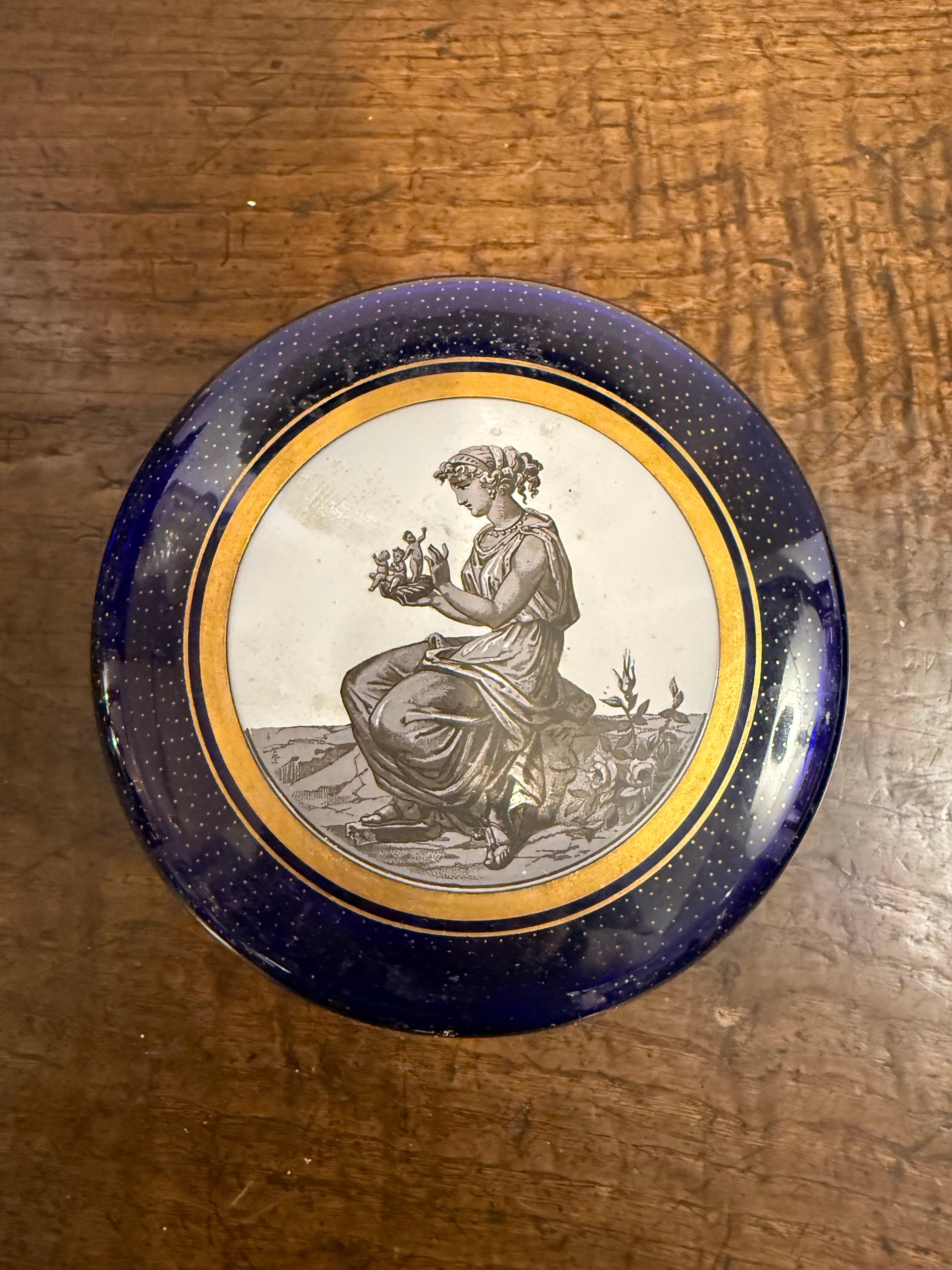 A Cobalt Blue Gilt Enamel Lidded Trinket Box, Early 20th Century
With classical pictoral ceramic inset and brass fittings

Provenance: Private Australian Collection.

Dimensions:
Height: 15.5cm.
Diameter: 15cm.