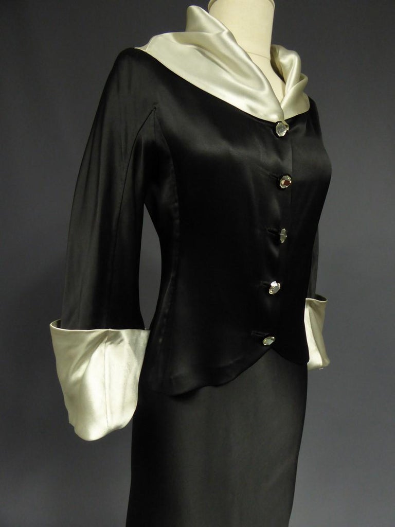 Circa 1933/1934
​Paris France

A reversible black and iridescent white satin silk Tuxedo skirt and jacket suit. Draped shawl collar, Pagoda wide cuffed sleeves. Sheath skirt with bias cut and split on one side. Buttons in black galalith and crystal