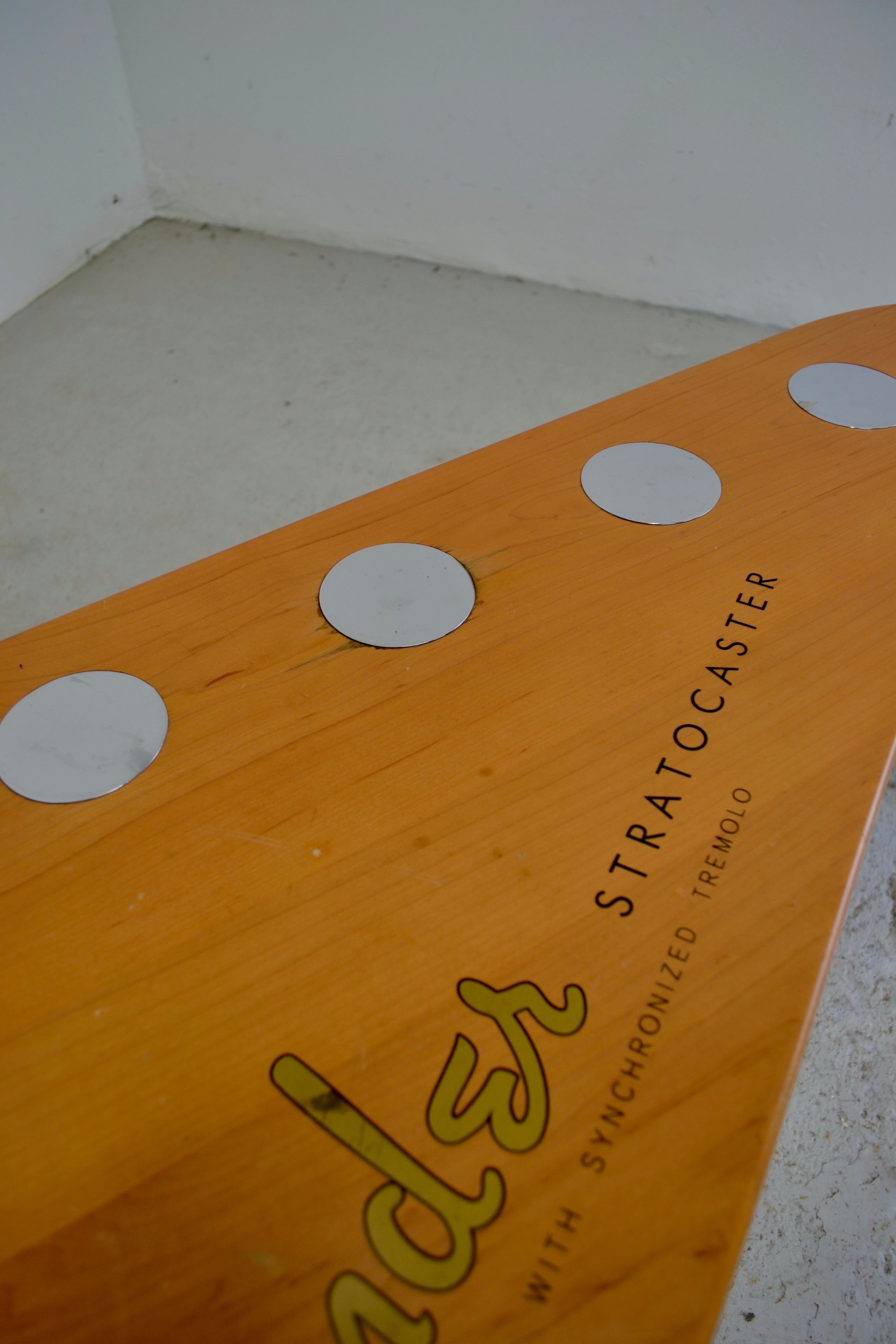 A unique coffee table in the shape of a Fender Stratocaster headstock, crafted from wood with a glossy finish, adorned with metal inlays, and supported by three sturdy metal legs. This rare model, manufactured under official Fender license, features