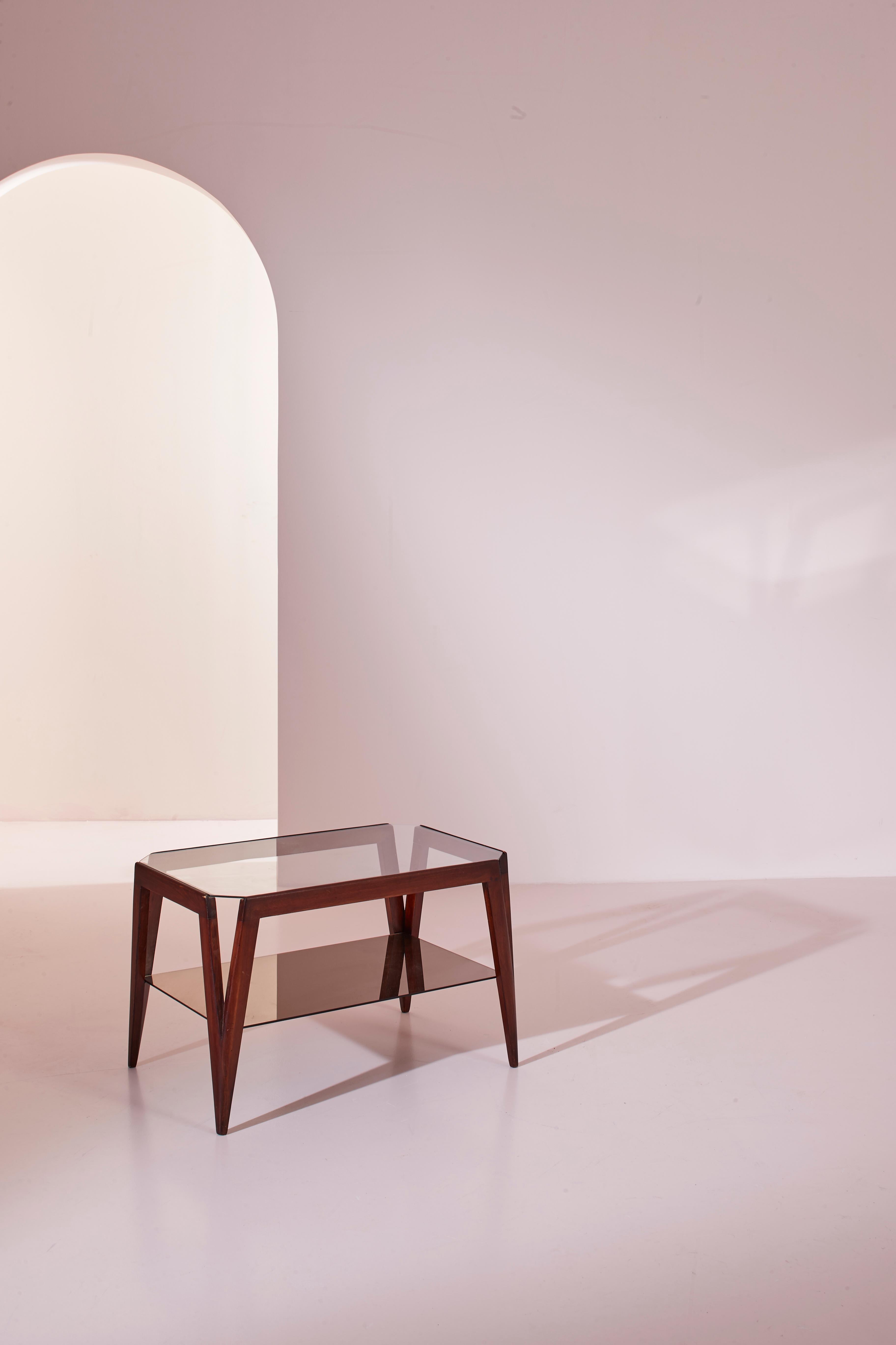 Cette belle table basse, fabriquée en Italie dans les années 1950 en bois teinté de noyer et en verre, apparaît comme une pièce où l'on dirait qu'un crayon a tracé joyeusement une succession rapide d'angles et d'arêtes aigus. Celles-ci ont