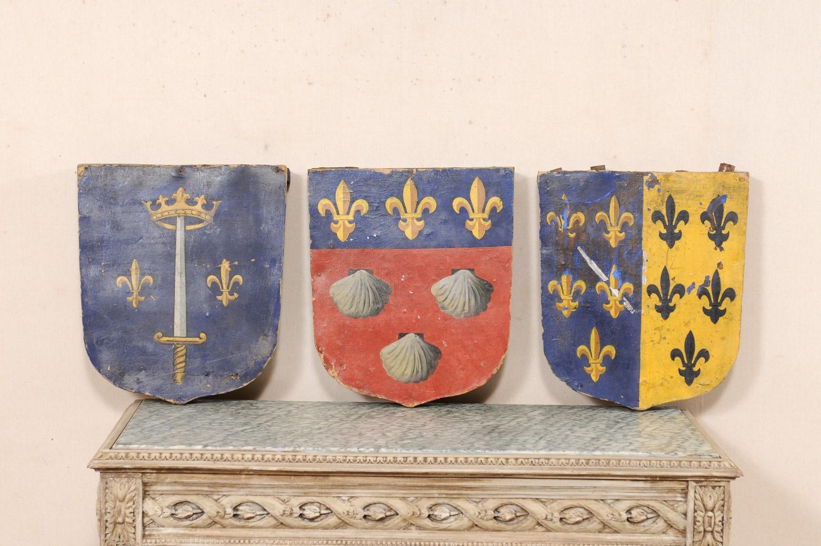 A French set of three processional plaques from the 19th century. These antique processional candle-holder plaques from France each have a shield shape design and feature their original hand-painted finish in a motif of fleur de lis, sword, crown