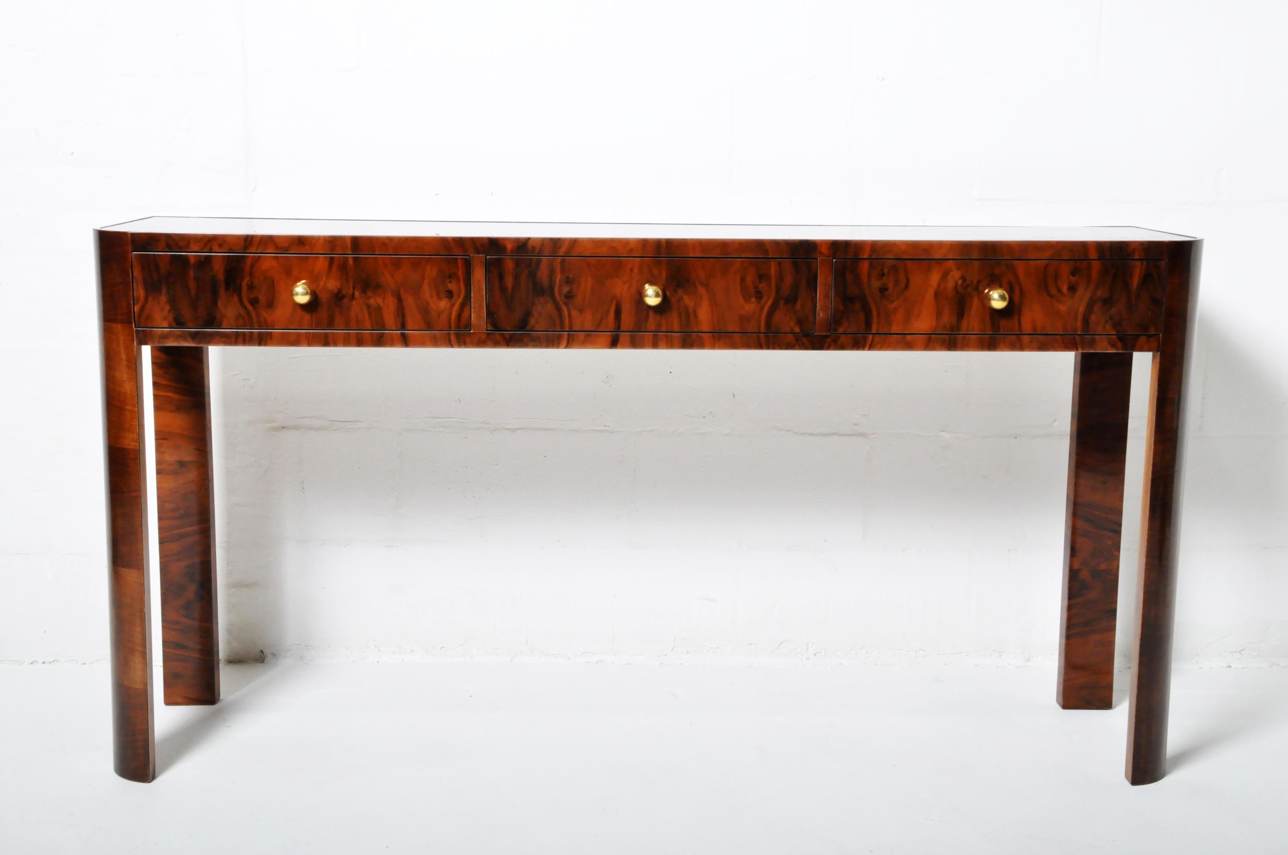 A classic Hungarian Art deco console table with three drawers, walnut veneer and a black glass top. Large round brass knobs add visual interest. Hungarian Art Deco is very similar to French art Deco but tends to be simpler and employs fewer exotic