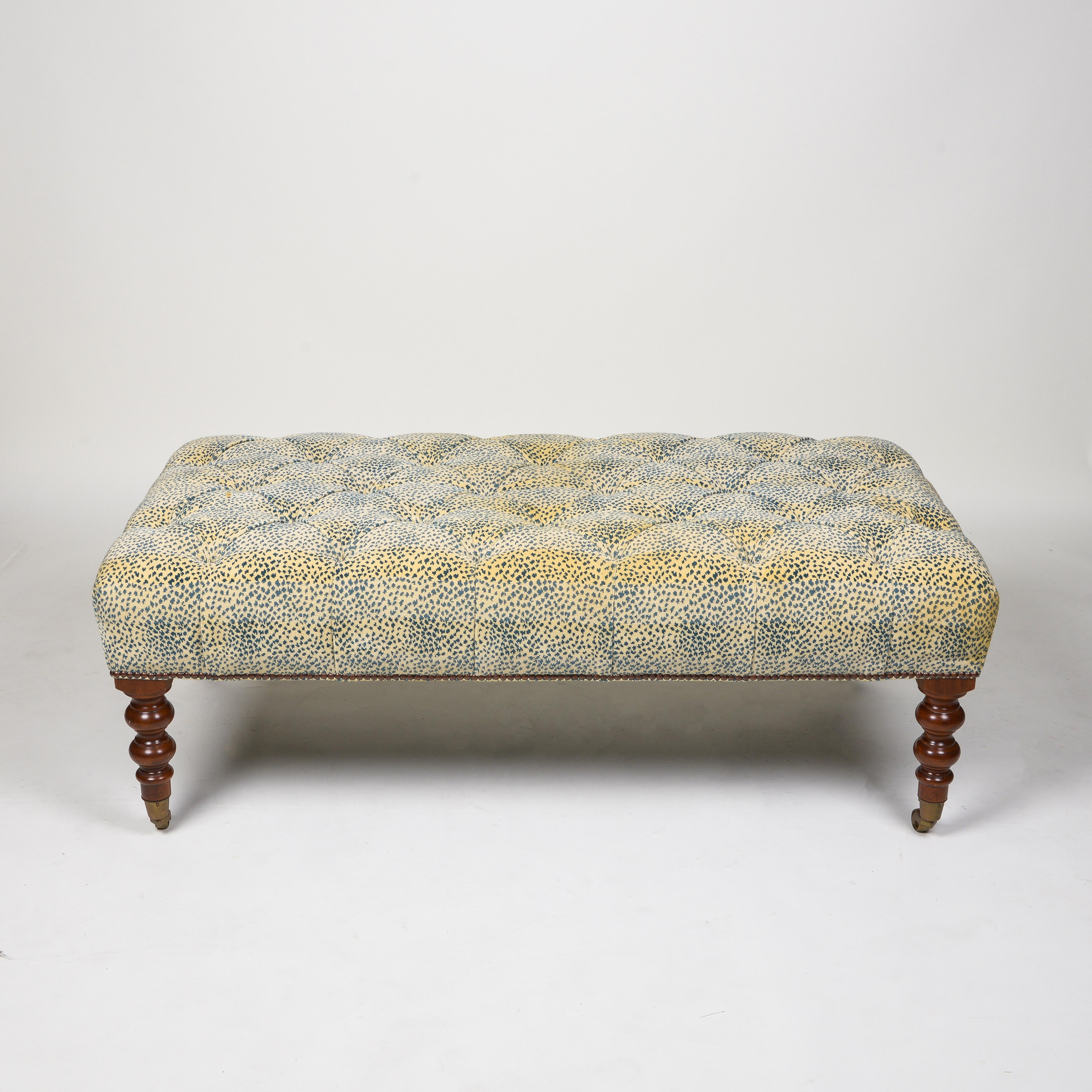 Upholstered in creamy yellow chenille with cobalt spots, tufted and accented around the base with brass nailheads; raised on turned legs terminating in brass caps and casters.
