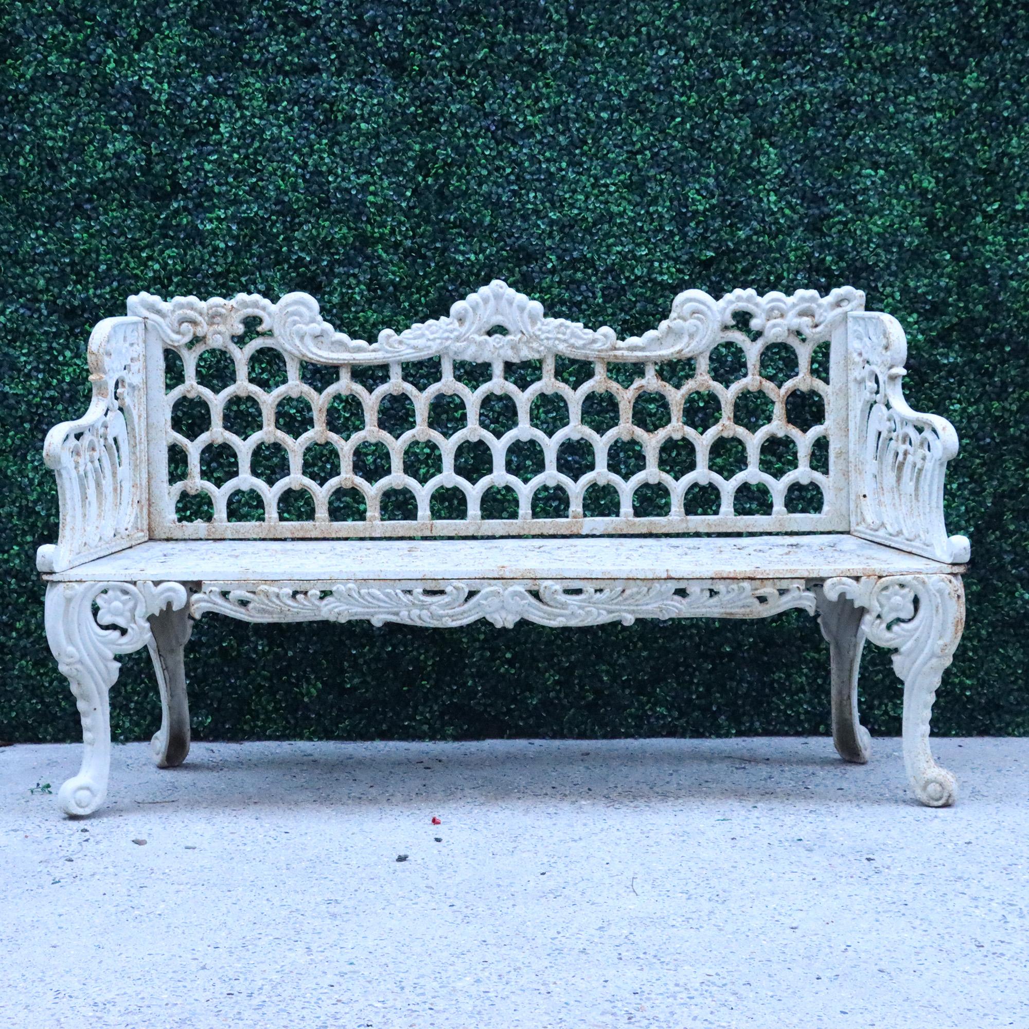 A contemporary cast iron garden bench in white. Floral and scroll design crest rail over arch. Decorated back flanked by stepped arms above seat supported on cabriole legs.