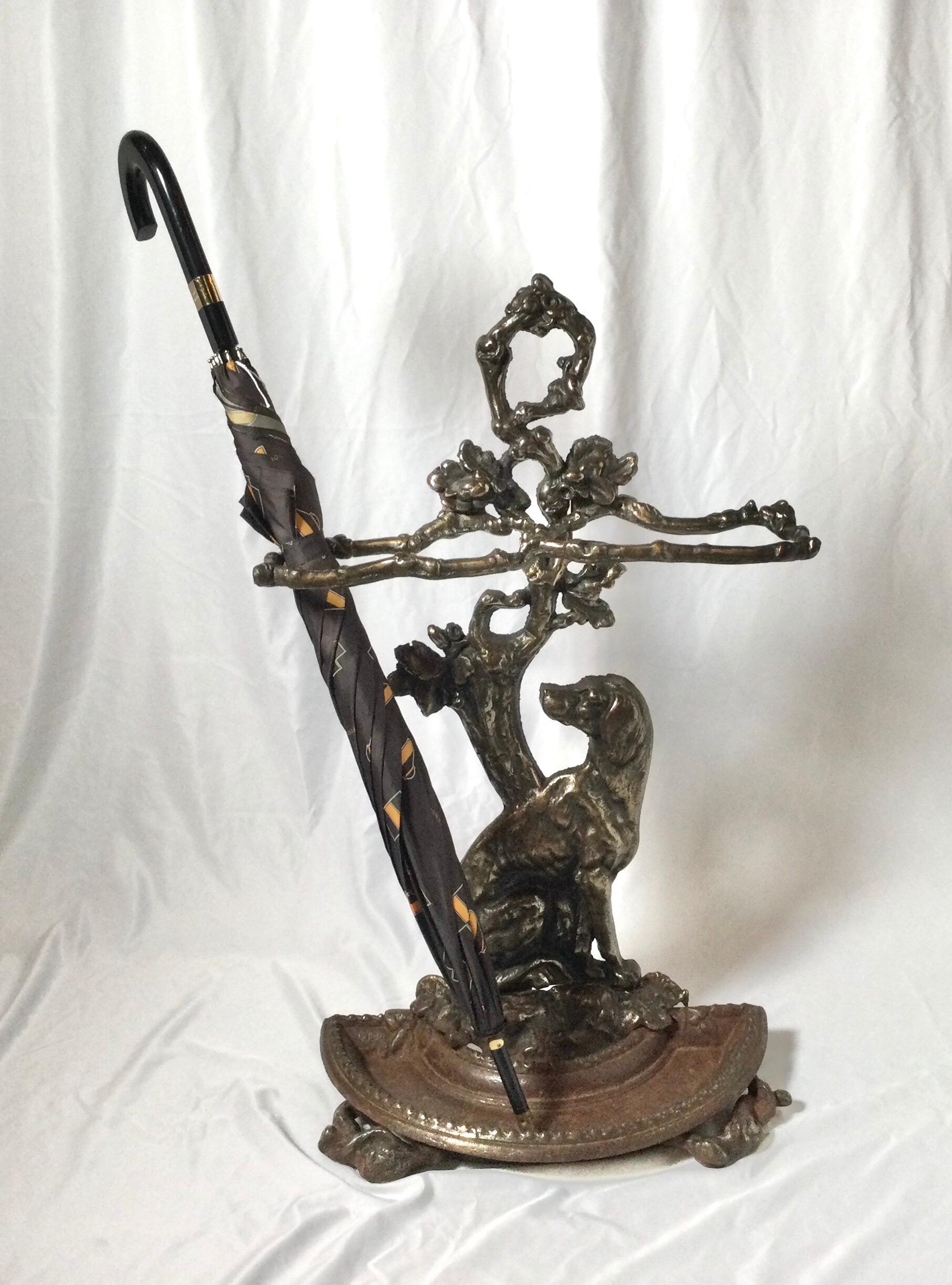 A cast iron umbrella stand with a patinated bronze finish. The stand with a shapely branch form with a sporting dog at the base.