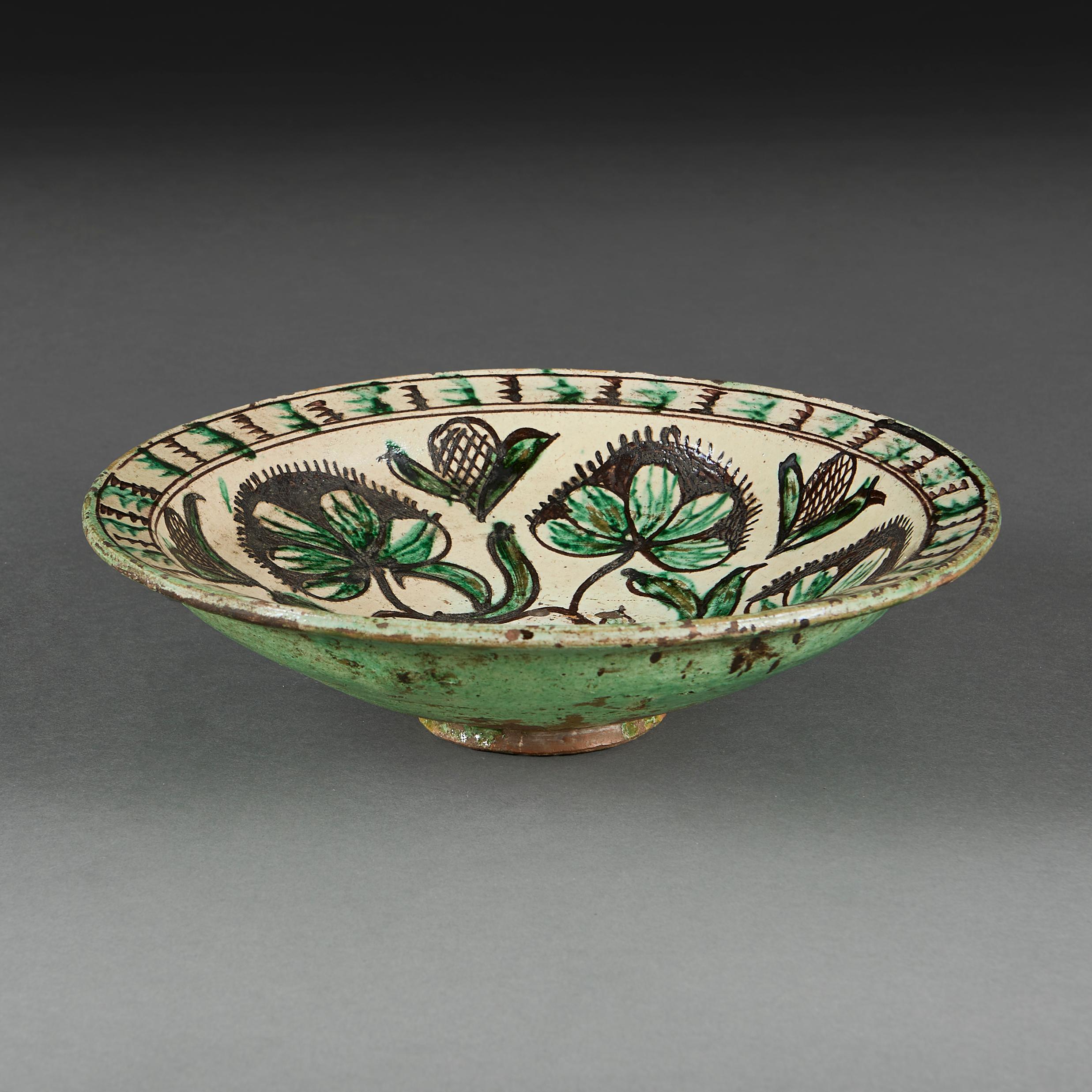 Chargeur du début du 20e siècle décoré de motifs feuillagés dans les verts et les bruns, et d'arabesques imbriquées, le dos étant recouvert d'une glaçure verte unie.