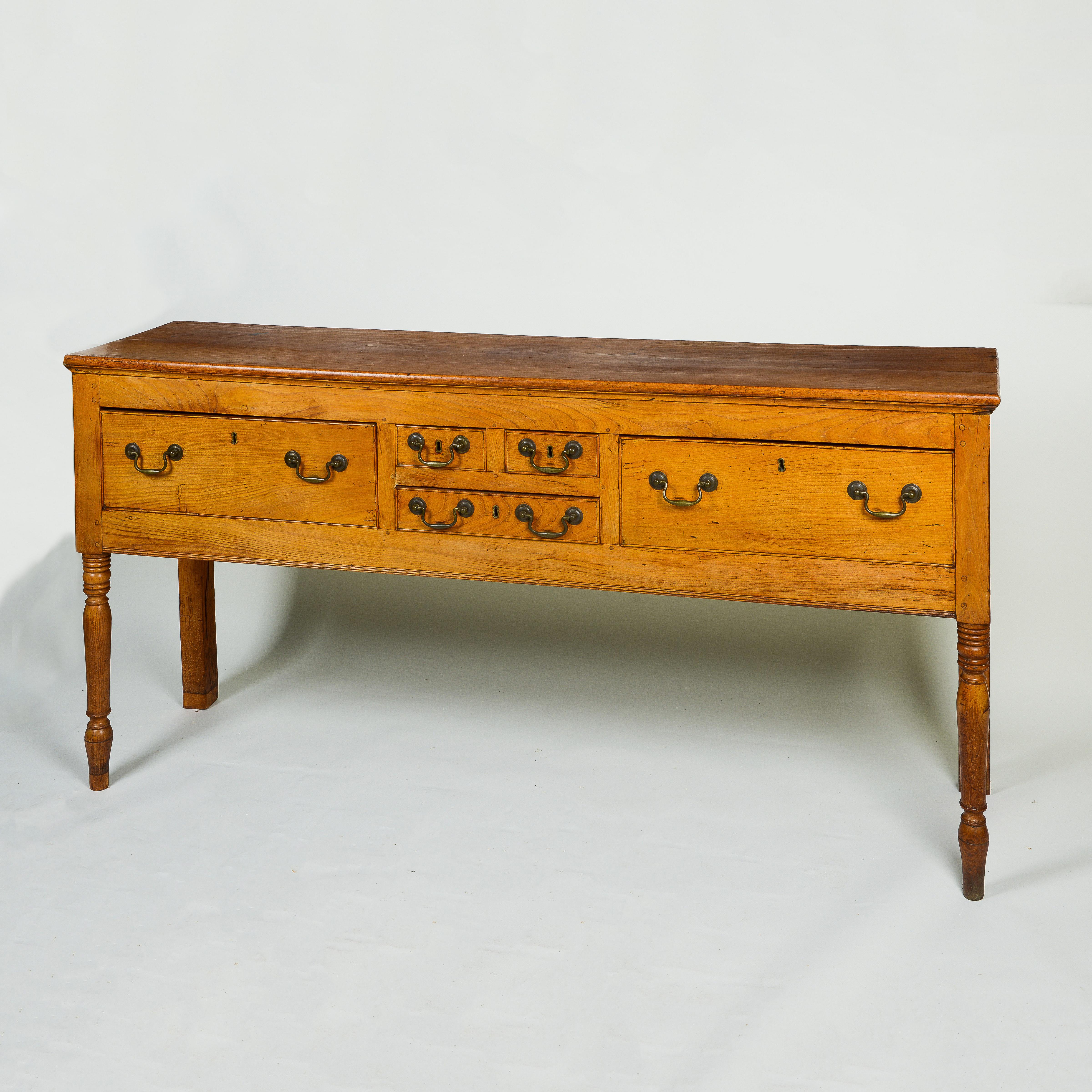 The rectangular overhanging top over a deep frieze fitted with five drawers mounted with brass bale handles; raised on front ring turned legs.