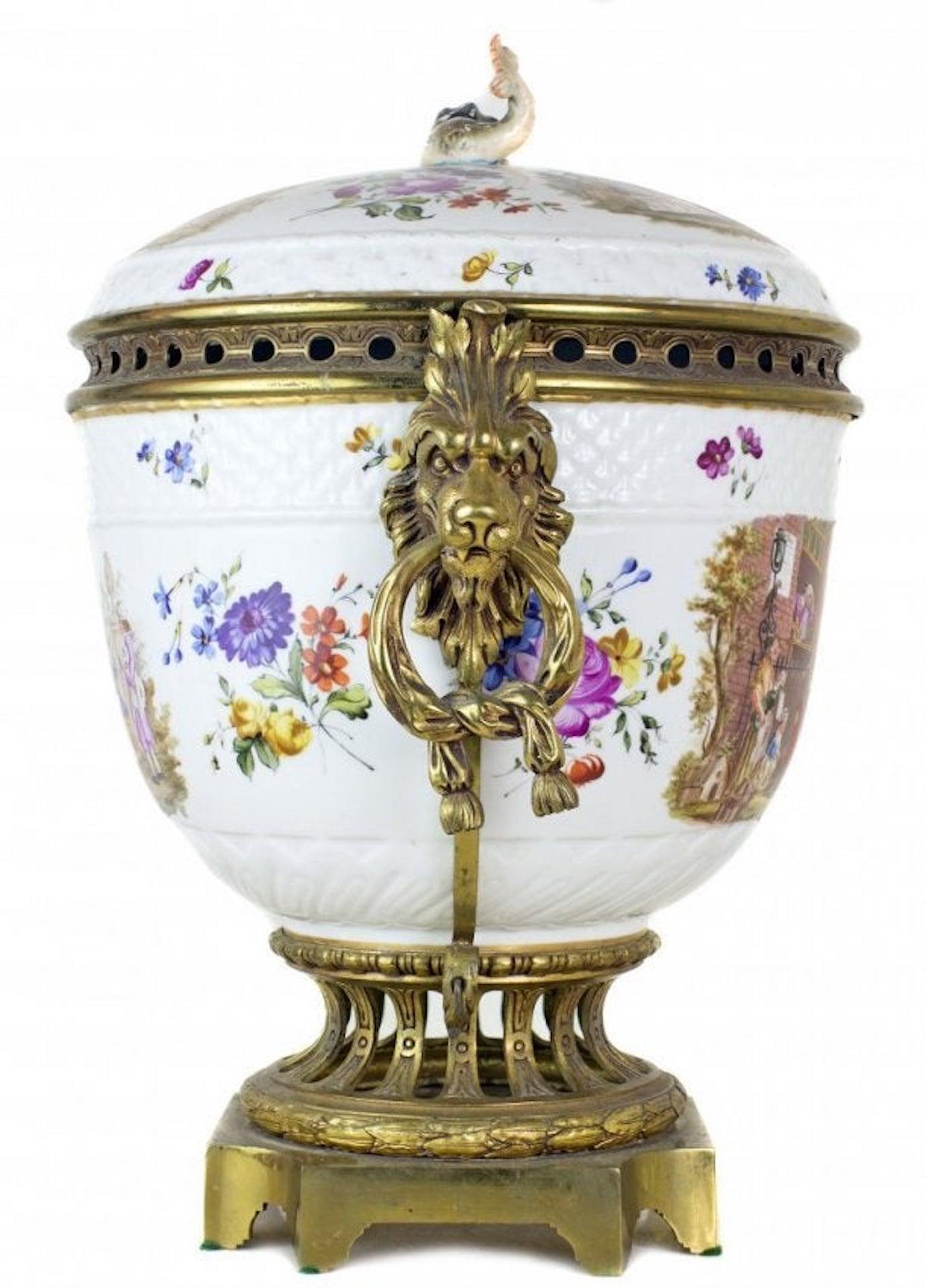 A continental gilt-bronze mounted porcelain potpourri
late 19th century,
the large round-form body topped by a domed lid and dolphin finial, the whole painted with satiric dinner scenes, fitted with a pieced rim flanked by lion's mask and ring