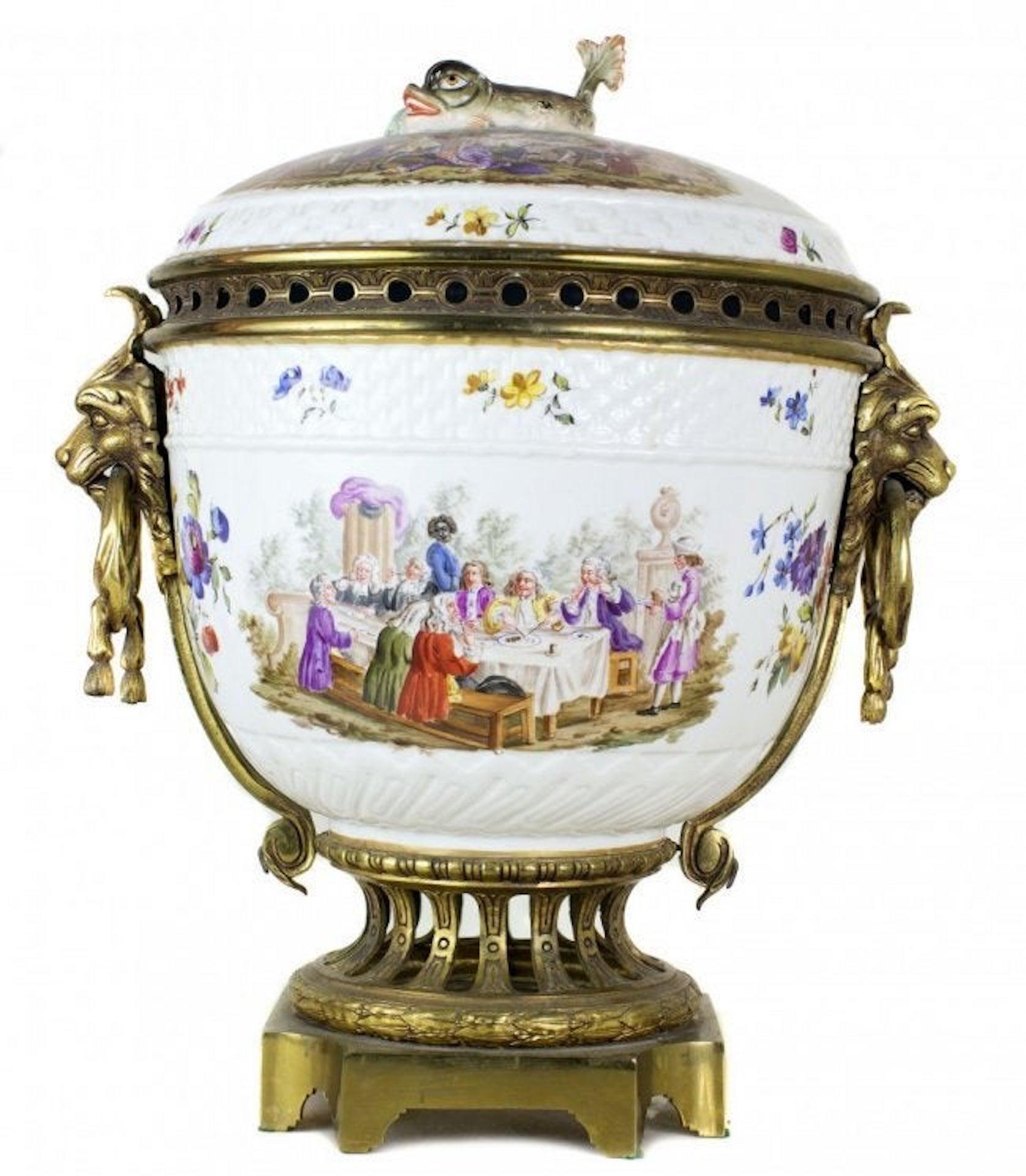 A continental gilt-bronze mounted porcelain potpourri
Late 19th century,
The large round-form body topped by a domed lid and dolphin finial, the whole painted with satiric dinner scenes, fitted with a pieced rim flanked by lion's mask and ring