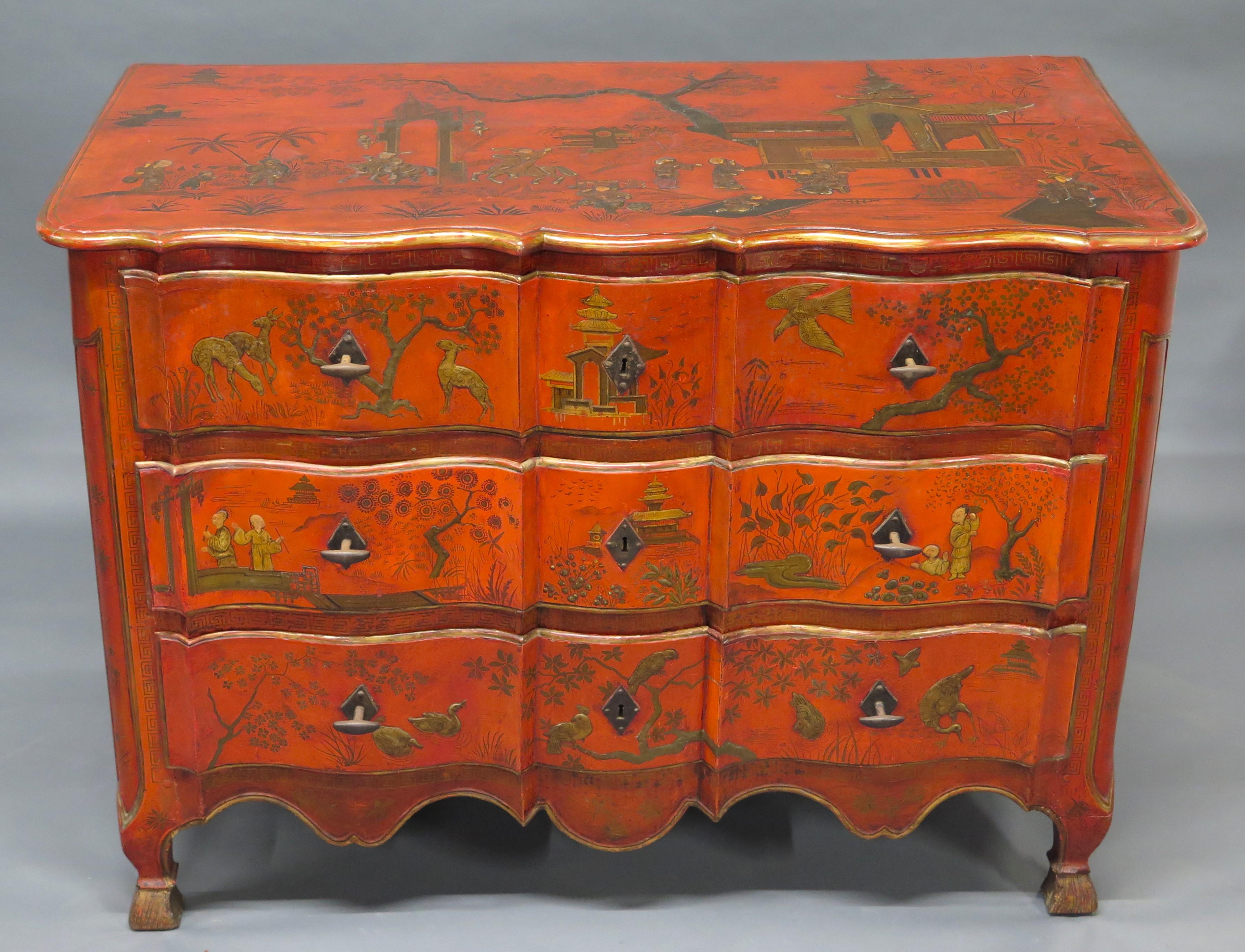 a Continental red chinoiserie decorated commode / chest of drawers, the shaped top with a scenic figural landscape, above the three conforming drawers further decorated with figures and flora and fauna, beautiful Greek Key borders, the paneled sides