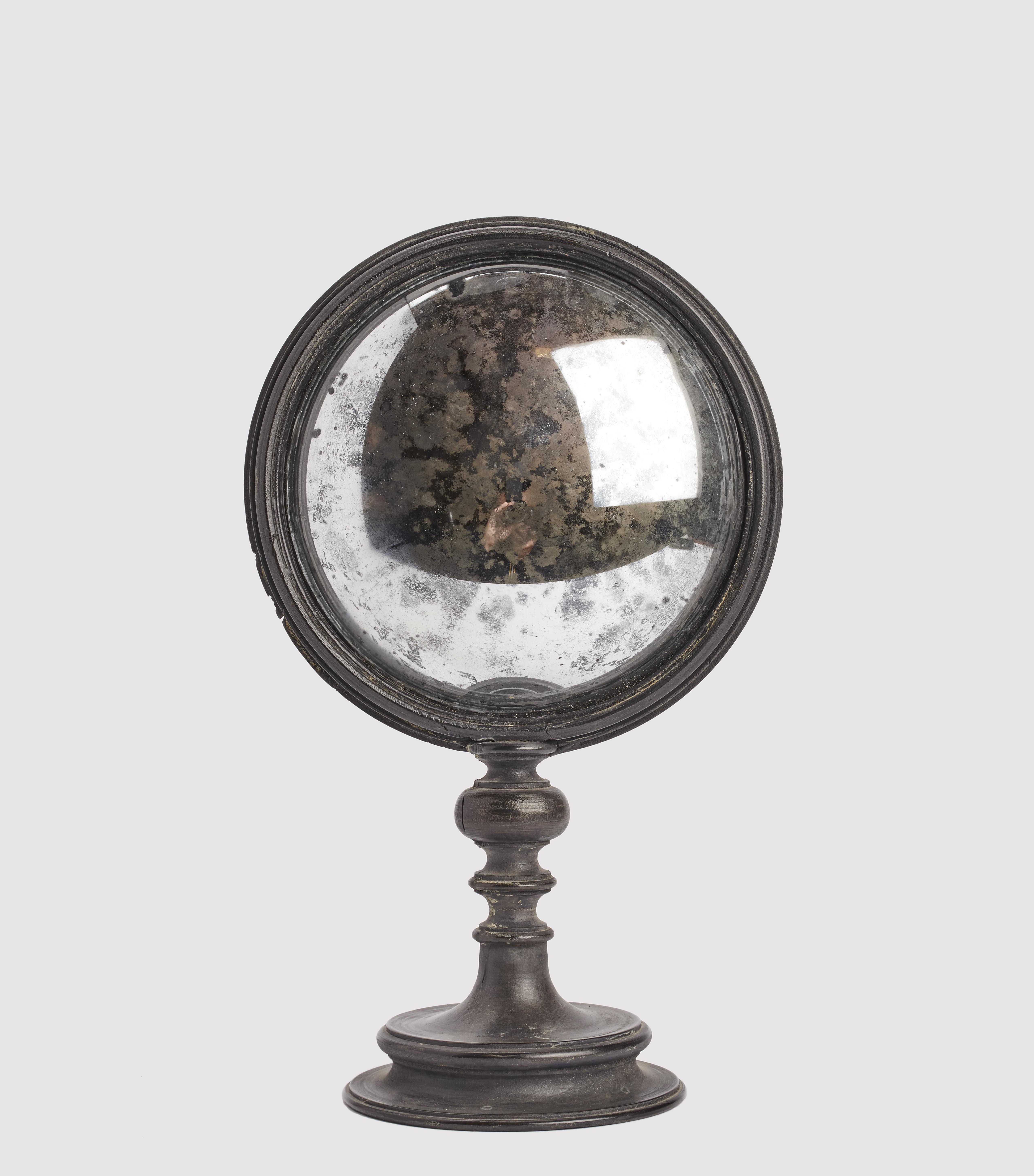 A Wunderkammer round convex mirror with black wooden frame mounted over a black wooden round base. On the rear of the frame there is one round mother of pearl nacre stone. Italy second half of 19th century.