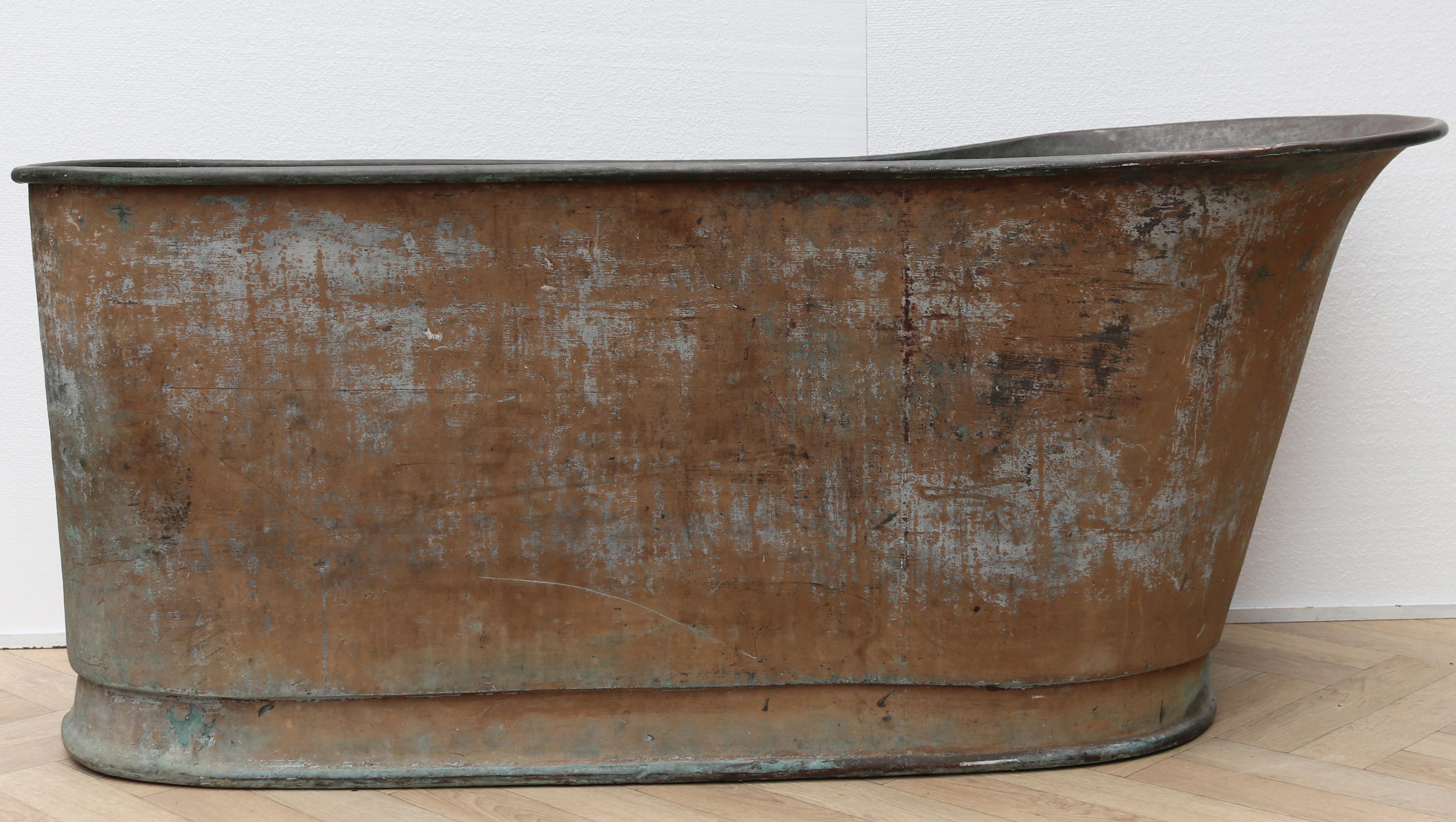 A large antique copper bathtub with a weathered verdigris and old paint finish.