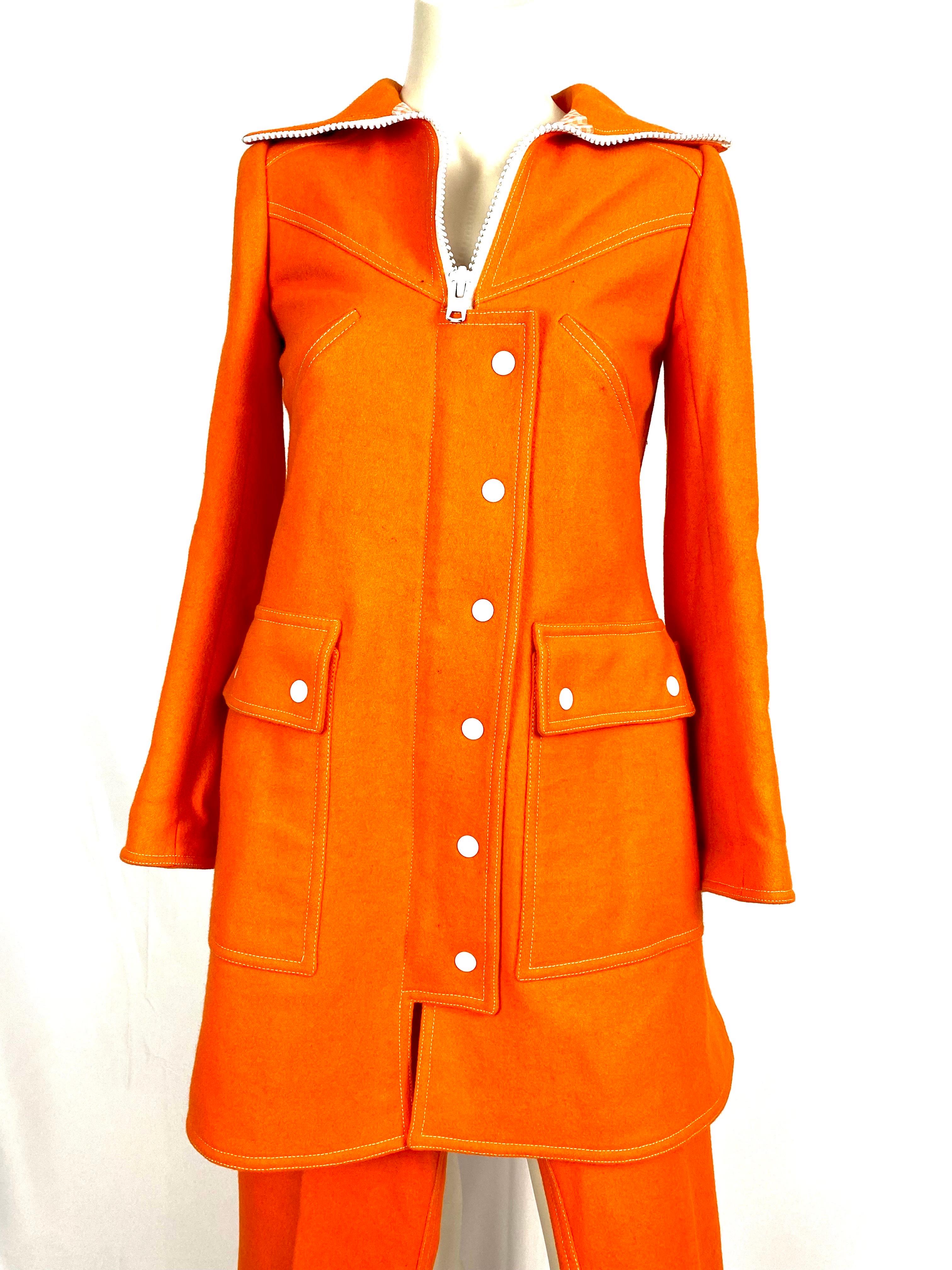 Vintage André Courrèges Hyperbole trouser suit numbered 0520940 from the 1970s.
In orange wool, fitted, pretty trucker collar with a long and imposing white zipper partly hidden by a press-stud flap.
2 raglan pockets on the chest.
2 large flap