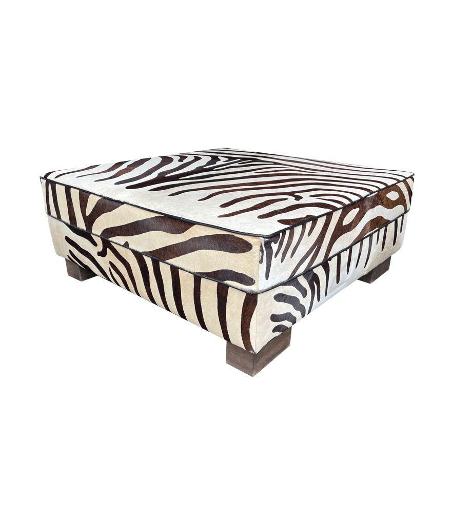 A cowhide covered ottoman with printed zebra skin design mounted on wooden feet. There is glass top so could be used as a coffee table or footstool ottoman.
