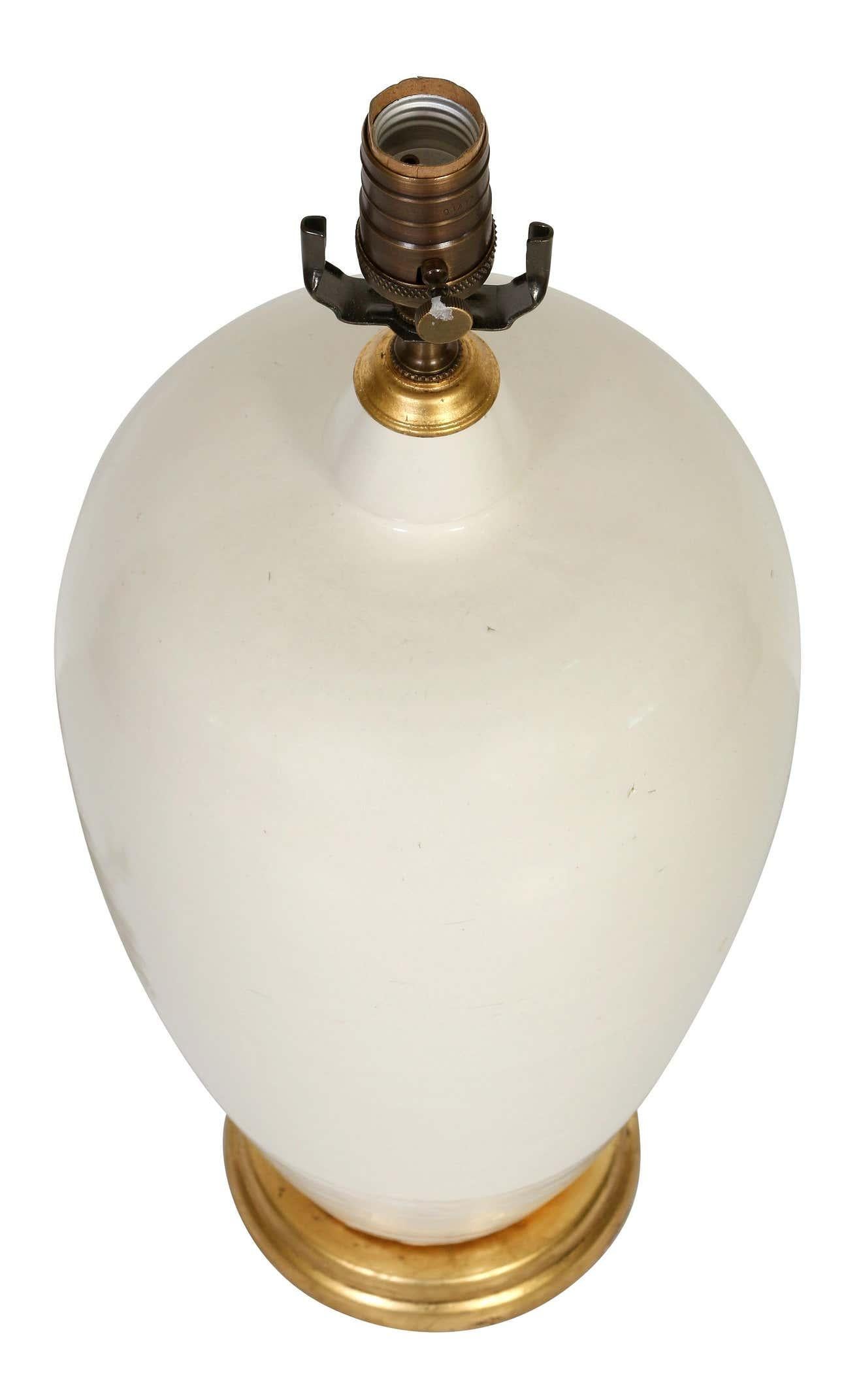 Eine Keramiklampe in schöner cremefarbener Glasur mit einer anmutigen Silhouette. Der warme Vergoldungsholzsockel verleiht der Lampe eine weiche Eleganz. Mit ihrer neutralen Farbe können diese Lampen überall eingesetzt werden.