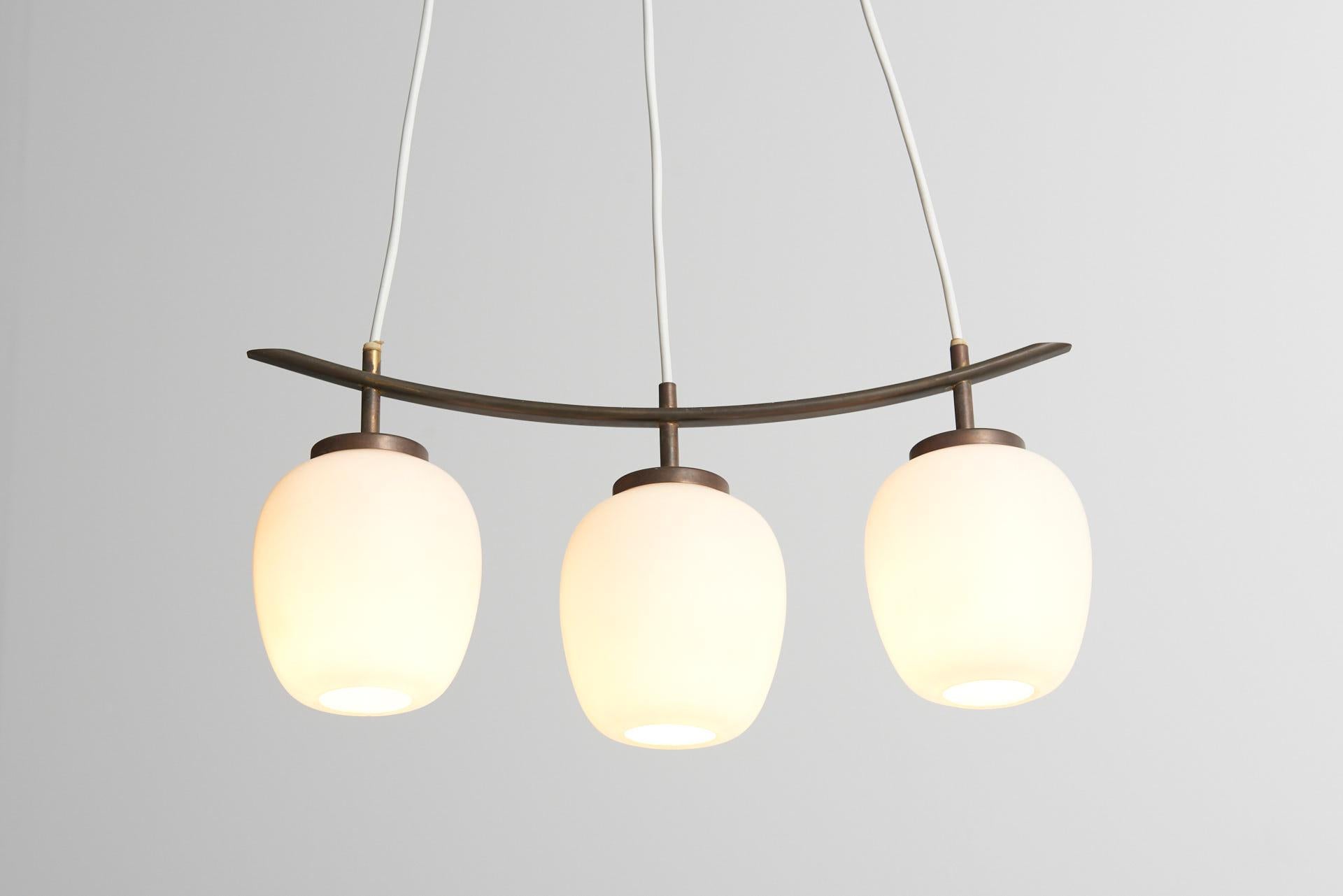 A rare pendant made of a curved brass frame with three opaline glass shades. Designed by Bent Karlby and made by chandeliers and pendants in Denmark, 1950s.