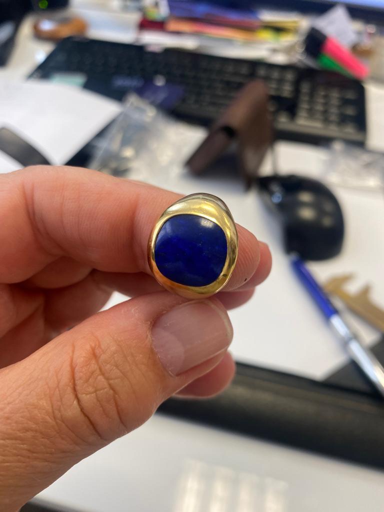 A cushion shaped Lapis Lazuli mounted in a 18ct yellow gold signet ring. Marked 750 and indistinguishable Italian control marks. Max width 12mm. Gross weight: 12.2 grams. Ring is resizable. Size: K1/2 (UK), 51 (EU), 5.75 (US), 16.1mm (inside ring