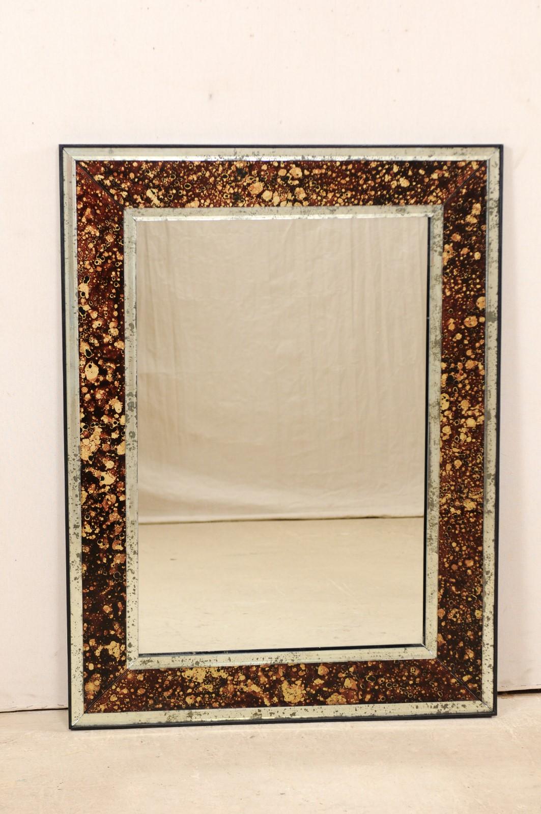 An American artisan made custom mirror with églomisé surround. This rectangular-shaped mirror features a fabulous faux tortoise églomisé surround, brown in color, framed within thinner antiqued mirror moldings. The tortoise coloring is primarily