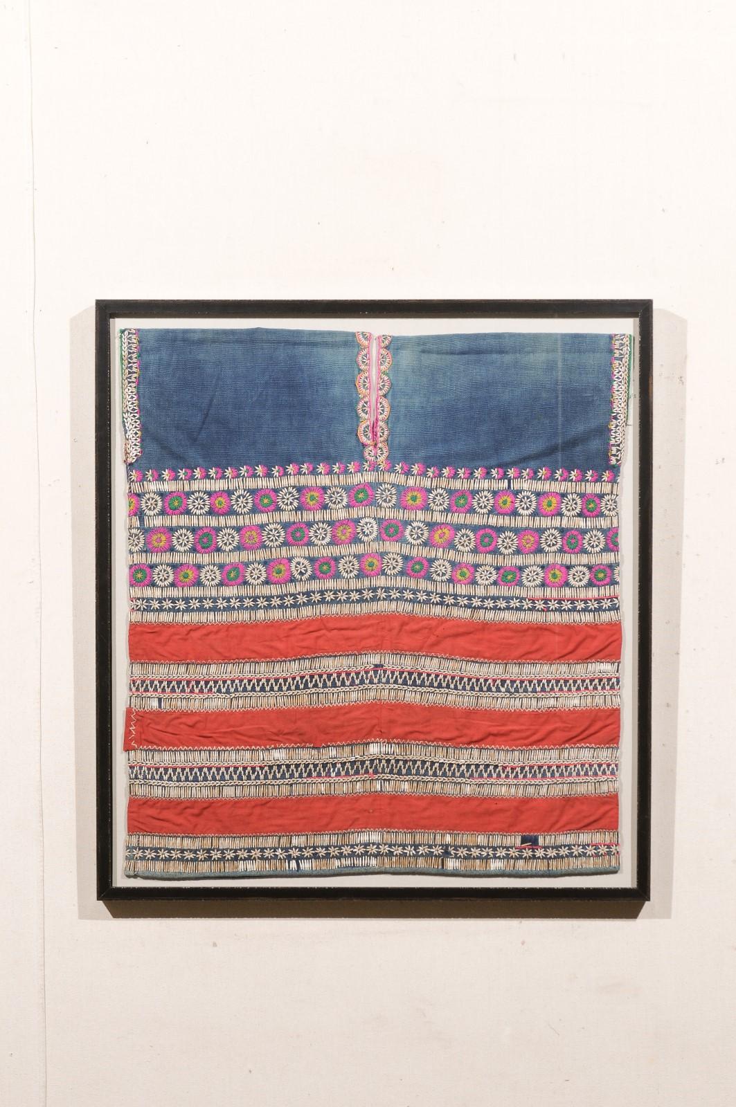 This custom framed wall art features a tunic from the Chin peoples of Burma (now called Myanmar), which has been custom framed. This early to mid 20th century tunic has a red cloth that looks like silk, along with an indigo dyed cotton, and