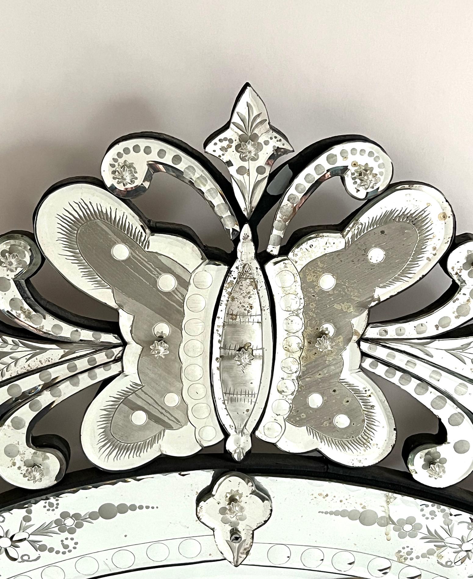 surmounted by an exuberant crest centering a boldly-scaled butterfly flanked by cascading floral vines; all over a circular mirror plate within a conforming beveled mirrored frame with reverse-etched floral and foliate vines; Established in 1911,