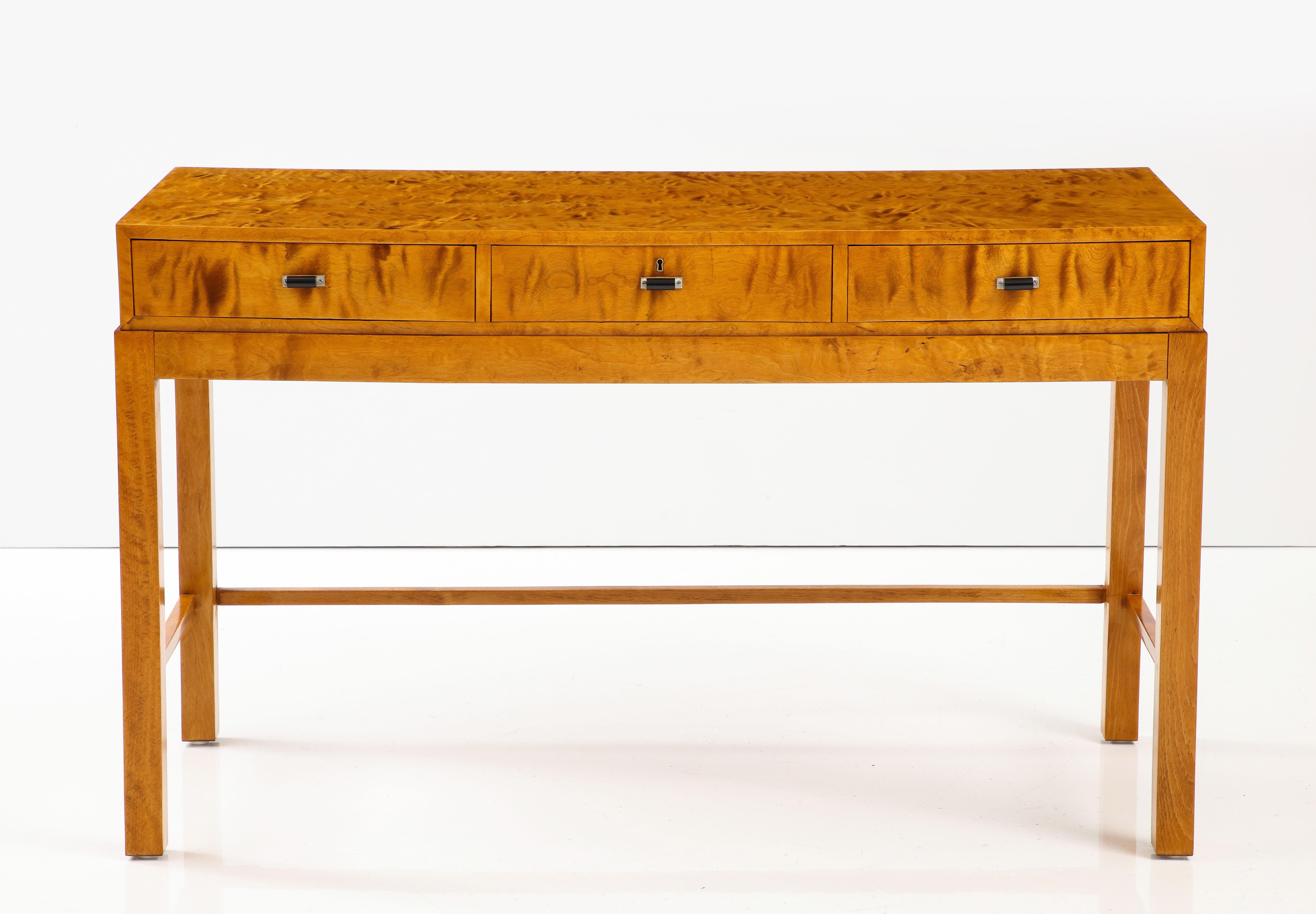 A Danish figured flamed birch console, Circa 1930-40, the rectangular top with three frieze drawers. The drawers with nickel and bakelite pulls. Raised on square legs joined by side and back cross -stretcher.