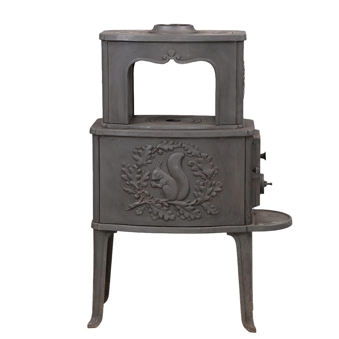 Poêle à bois autoportant en fonte du fabricant danois Morsø, avec des détails décoratifs classiques. Le devant est orné d'un relief représentant un écureuil entouré de feuilles de chêne, motif emblématique de la marque. La conception comprend une