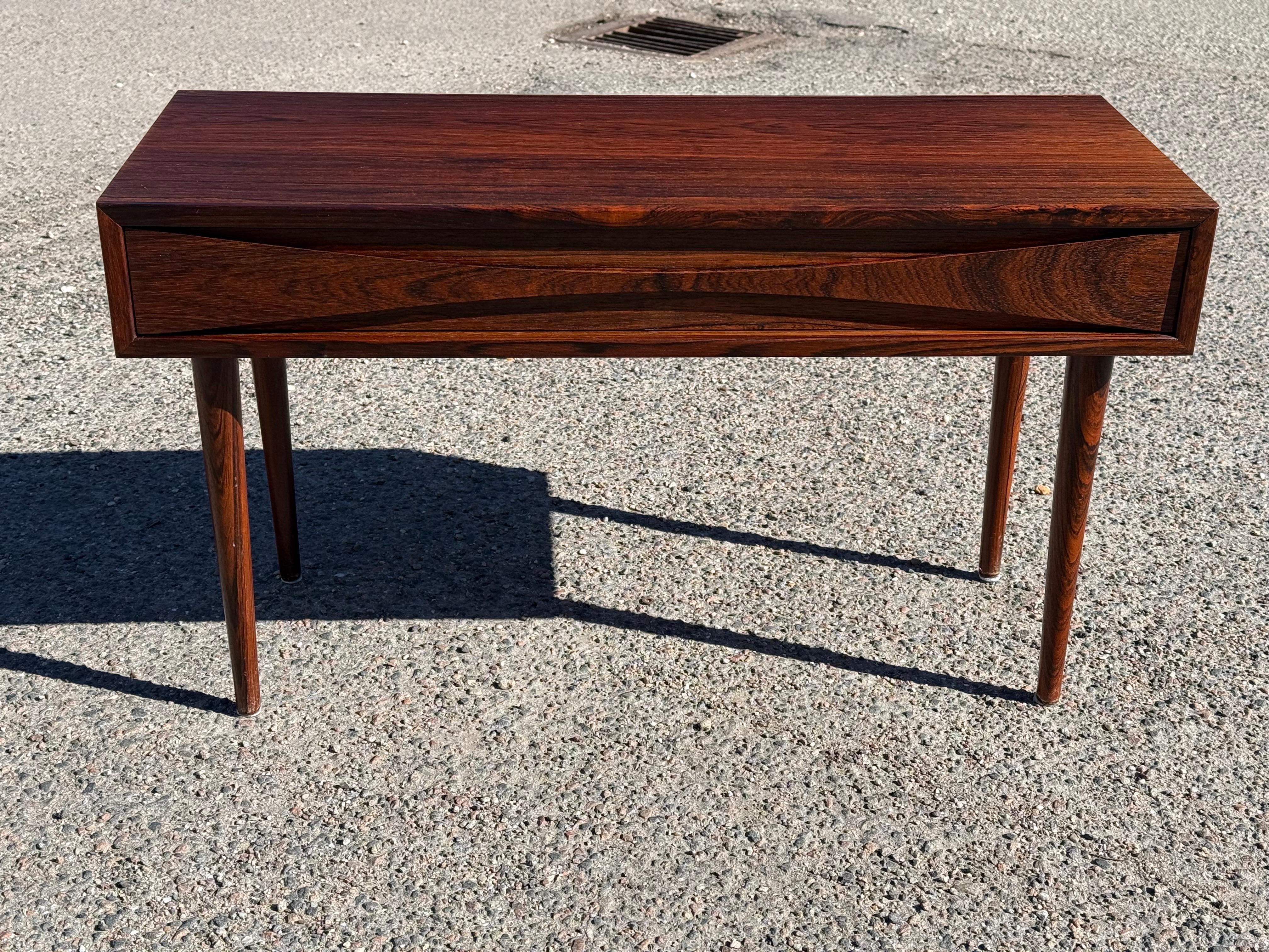 A rare gem of Danish modern design, this exquisite Arne Vodder design for Niels Clausen single-drawer chest table embodies elegance and functionality. Crafted by NC Møbler circa 1960, it features a rich dark wood finish, a beautifully sculpted