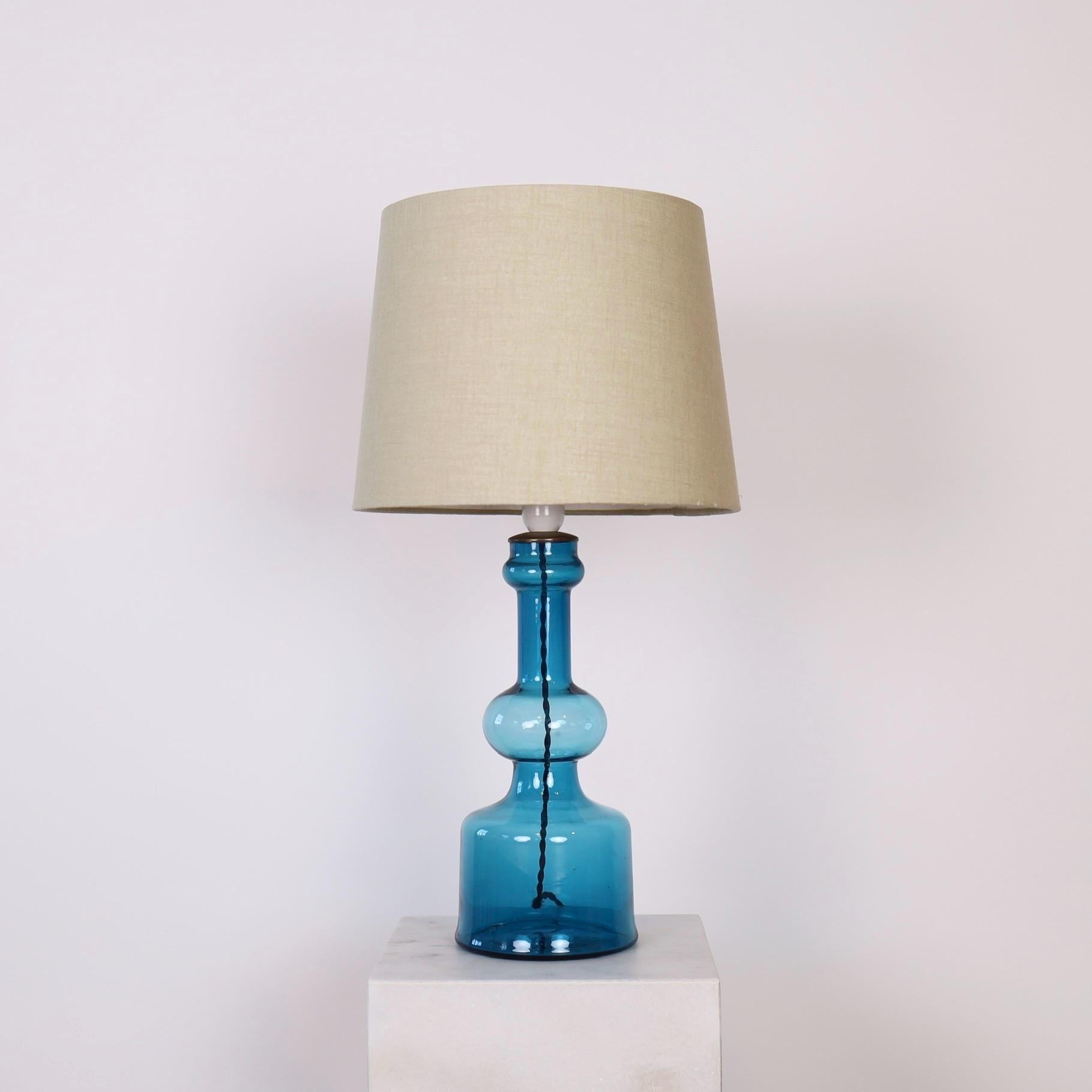 A light blue glass desk lamp designed by Lisbeth Brams in 1966 for Fog & Mørup. The eye-catching piece is one of three in her trio for Fog & Mørup. We have the trio available. 

* A light blue, transparent glass table lamp with a brass top and a