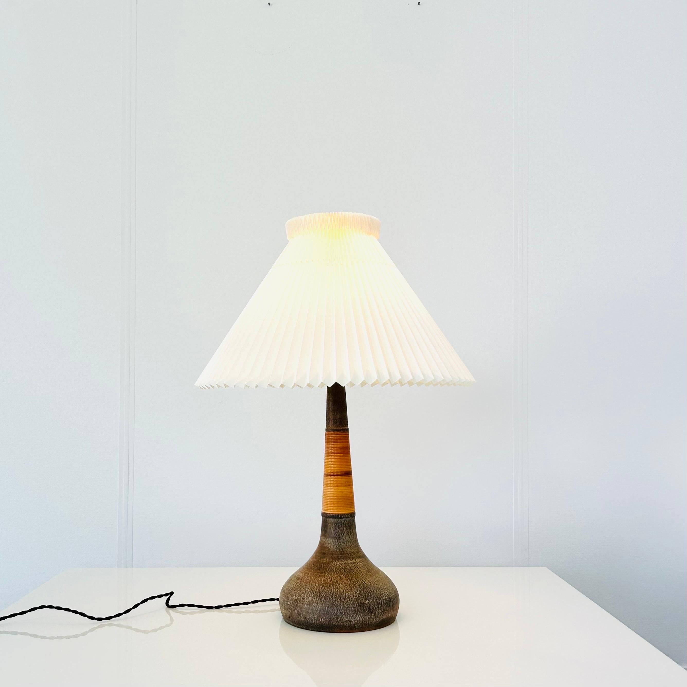 A ceramic table lamp handmade by Kähler for Le Klint in the 1960s. It is attributed to and most likely designed by Esben Klint (1915-1969). The lamp is made of unglazed ceramic wrapped with cane giving it stylish and warm look. 

The shade is a