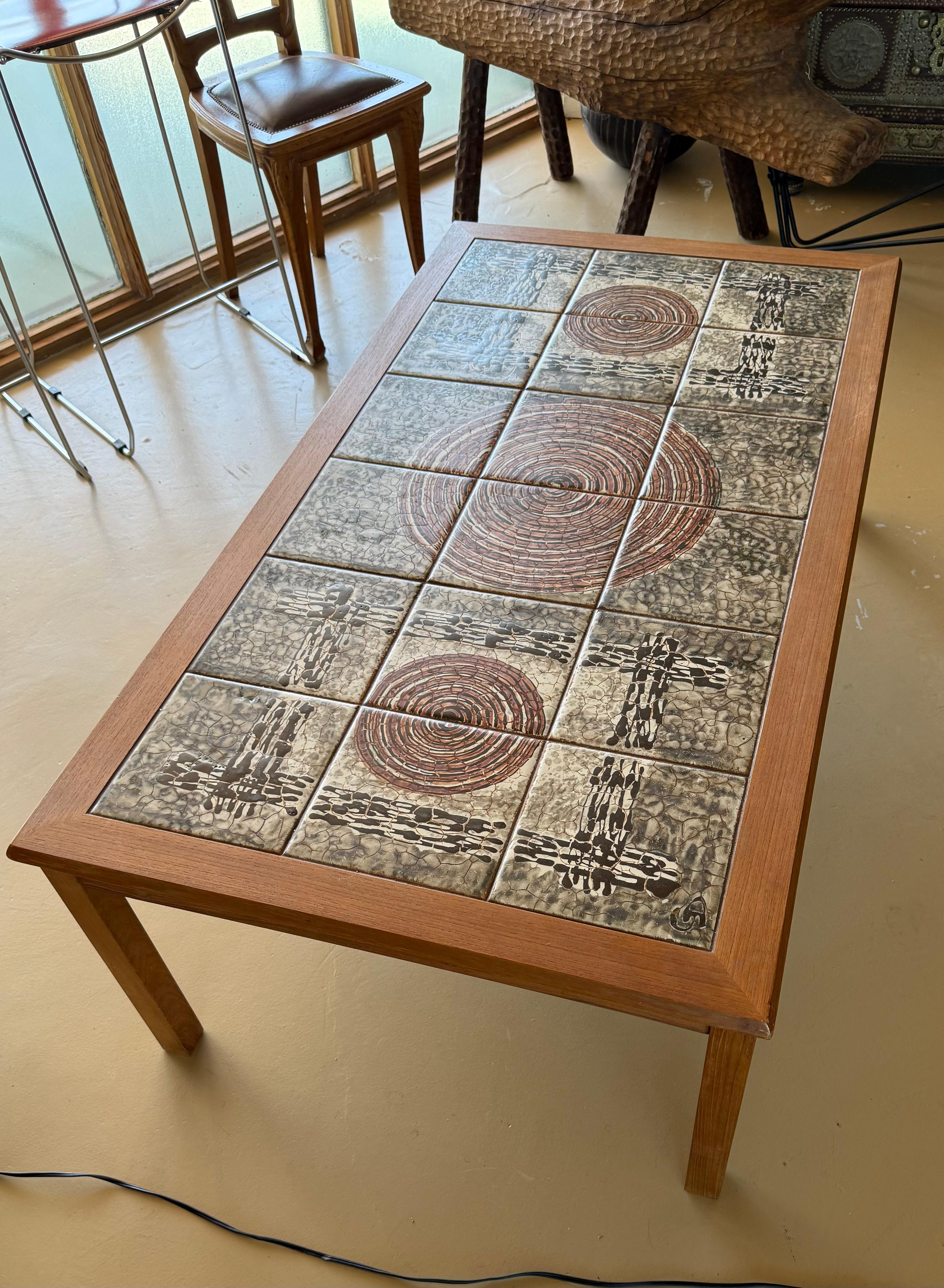 A mid century modern Danish teak coffee table with inlaid ceramic tiles, circa mid 1960s. Gorgeous warm wood grain in the teak, and the tiles boast tones of cream, burgundy, pewter, and licorice. Underneath table top is the maker’s mark stamp: “Made