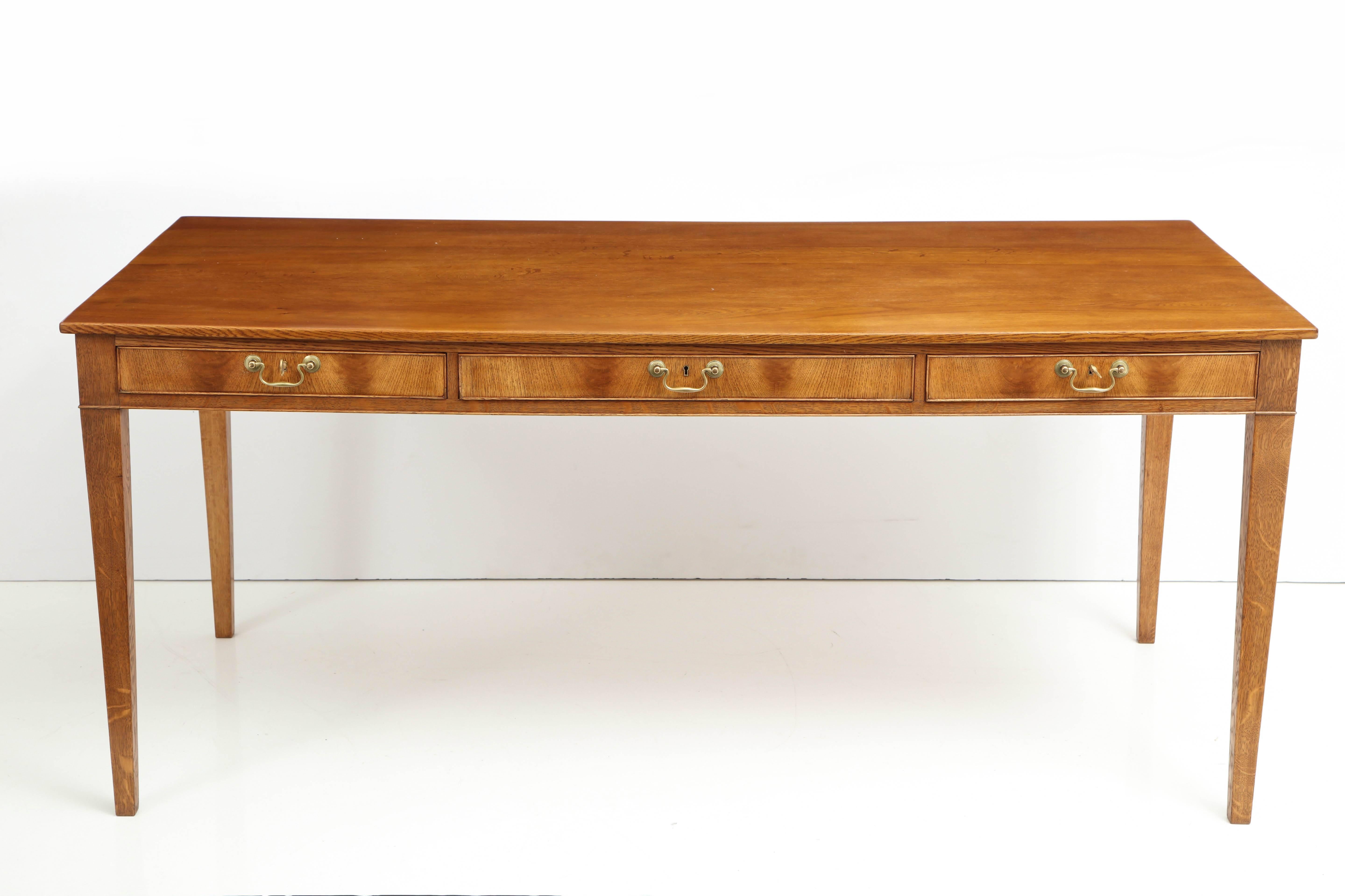 A large Danish European oak writing table by Frits Henningsen, circa 1940s, the rectangular top above a conforming frieze with three cock-beaded drawers with brass pulls, raised on square tapered legs.
