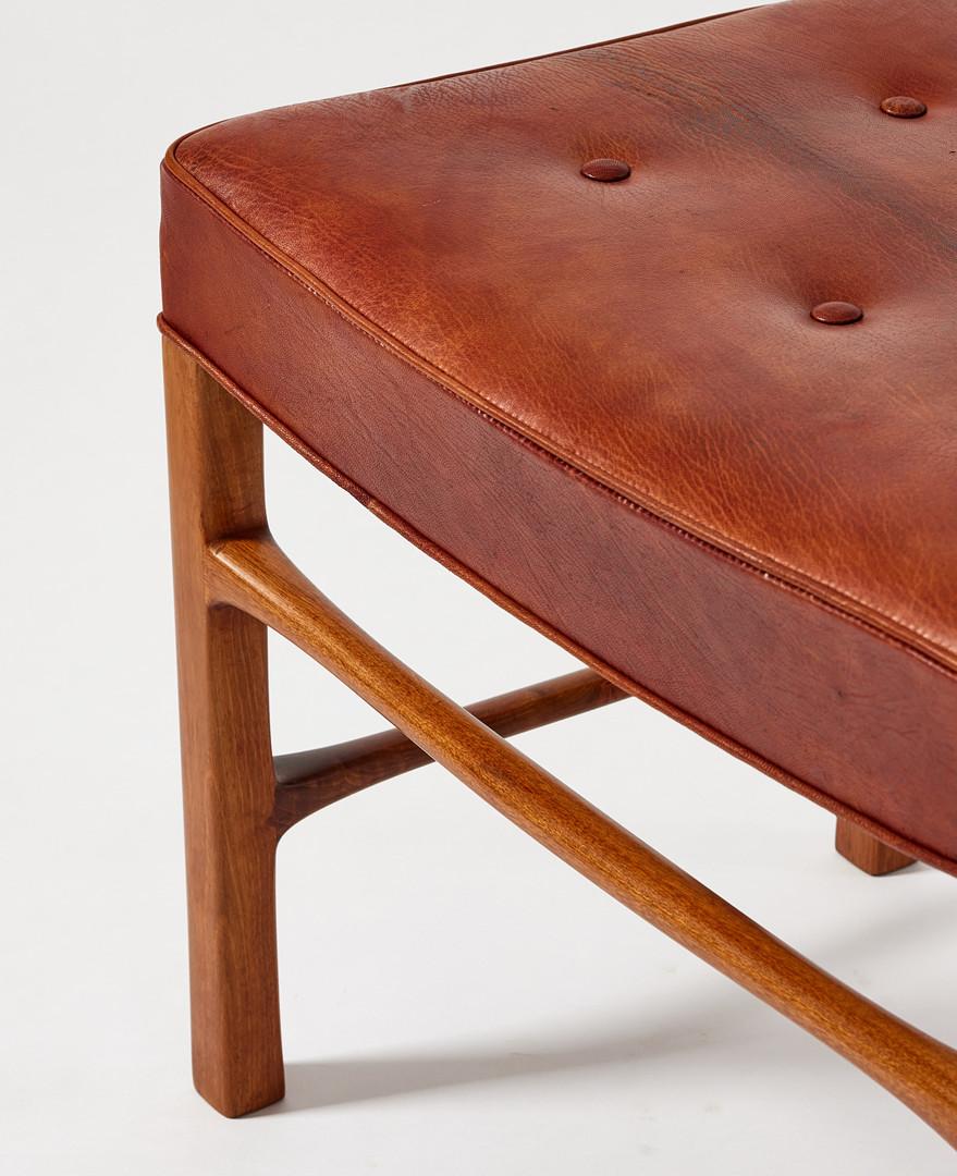 Banc danois rectangulaire dont l'assise est recouverte de cuir. Le cadre en teck a des jambes carrées reliées par des brancards de différentes hauteurs. Circa 1940