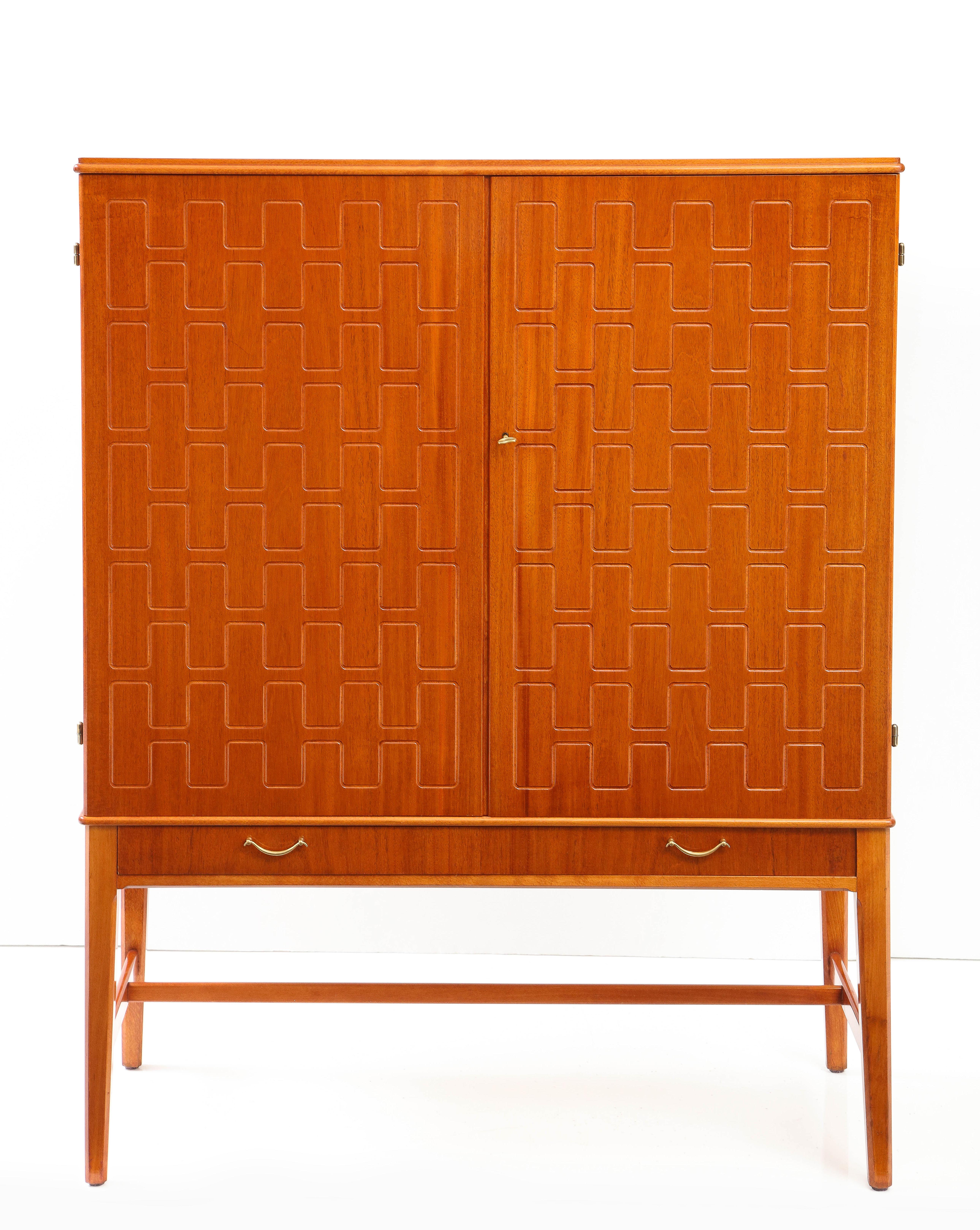 A Swedish teak and mahogany cabinet, Circa 1950s, Designed by David Rosén and produced by Svensk Möbelindustri. The rectangular top above two cupboard door with a classic relief carved pattern on the doors, above a long drawer raised on square