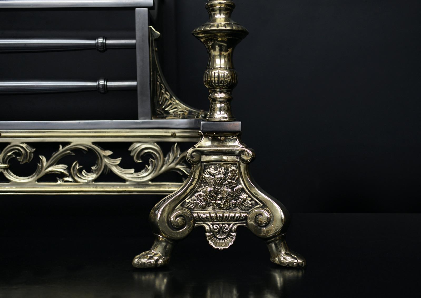 Una rejilla decorativa de latón y acero. Las patas, de latón, están coronadas por remates en forma de urna. La greca de fundición con volutas en toda la pieza, con barras frontales de acero pulido y remates de bola de latón liso encima. Trasera