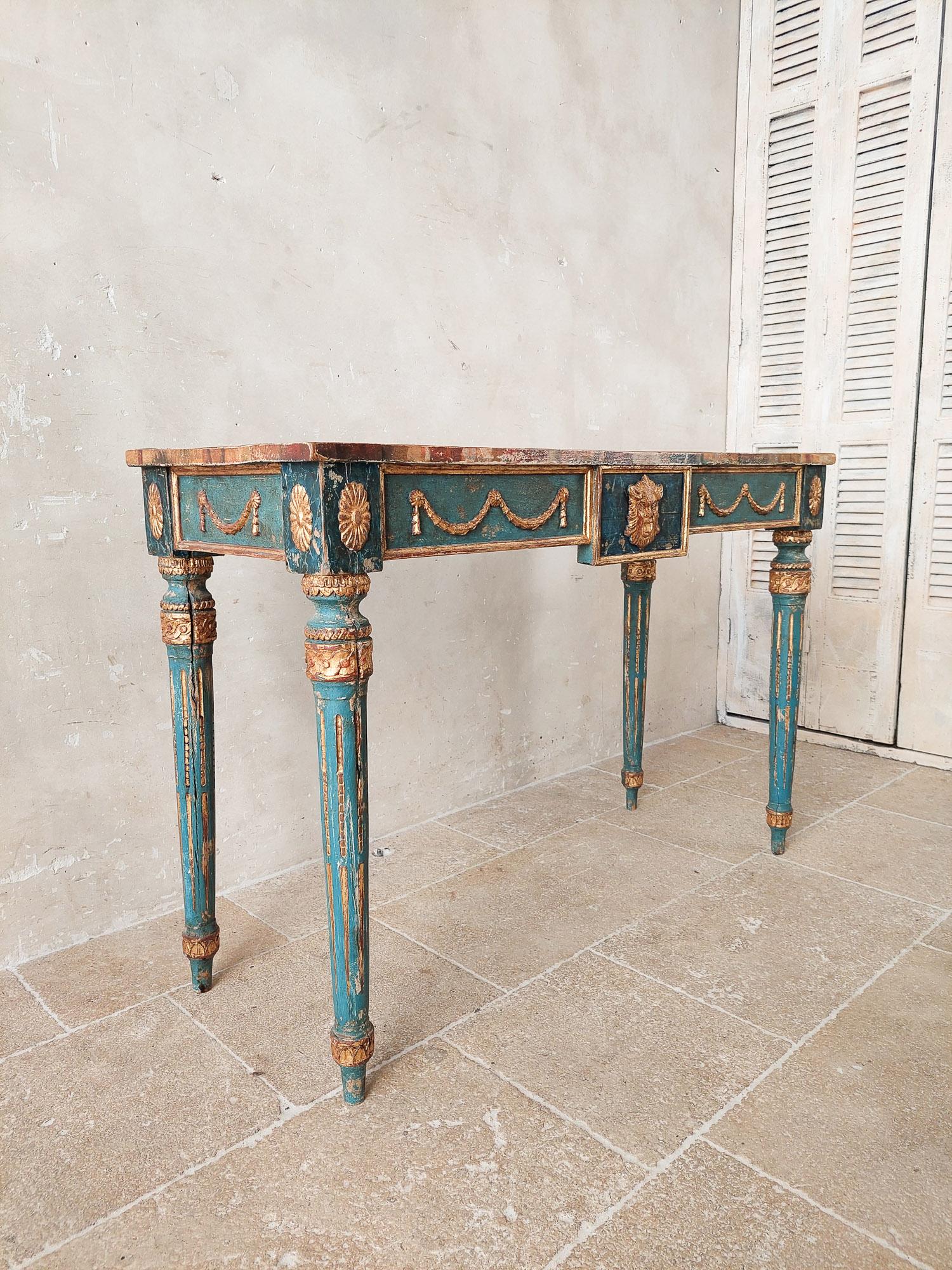An Italian Neoclassical console table patinated in blue, with golden details; guirlandes, rosettes and a lions head in the centre and fluted legs. Very attractive sidetable with painted faux marble top from early 20th century Italy.
