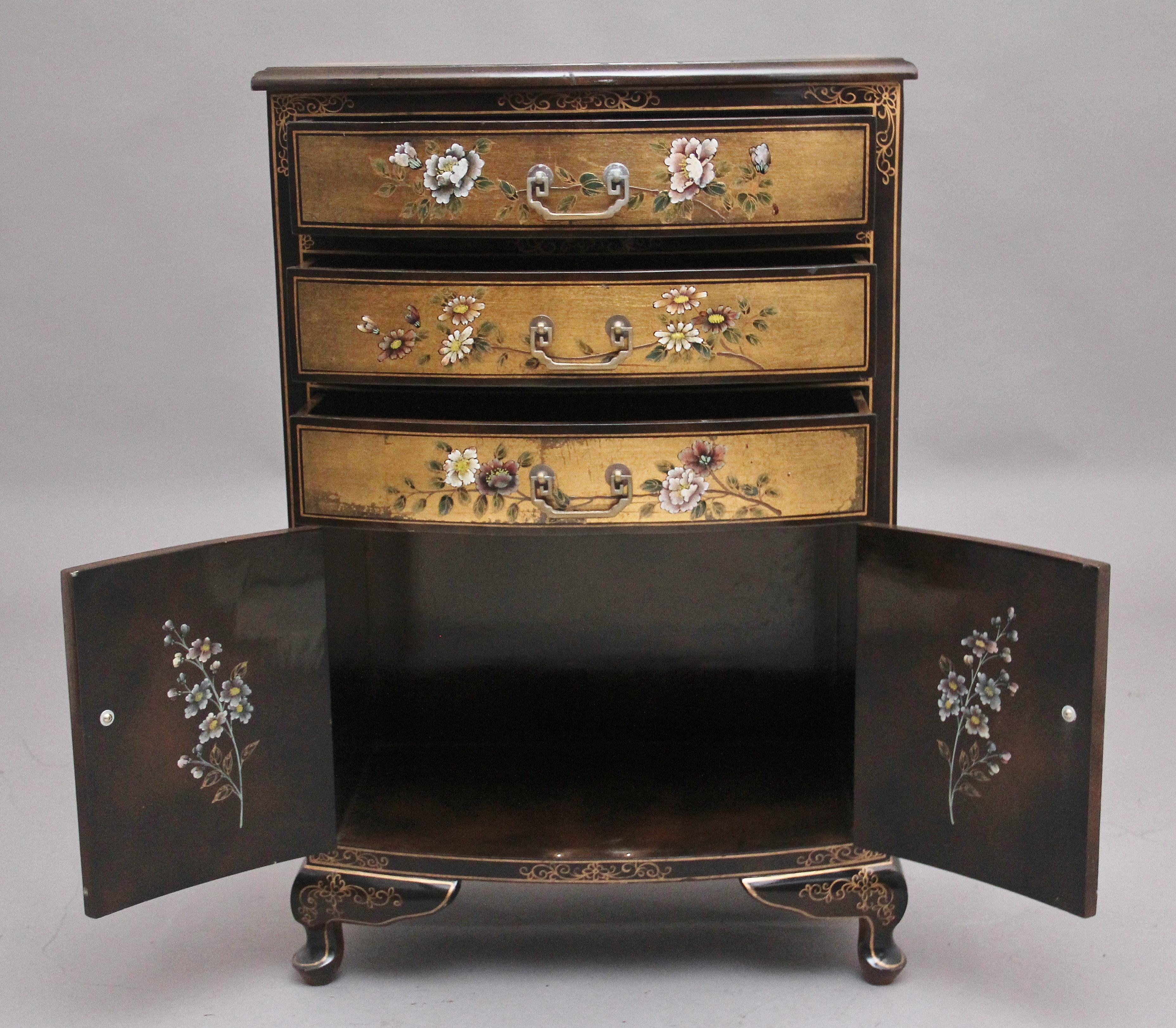 A decorative mid 20th century painted and lacquered cabinet, the shaped moulded edge top having a painted wildlife scene amongst a gold coloured background, the front having of the cabinet consisting of three drawers above a two door cupboard, the