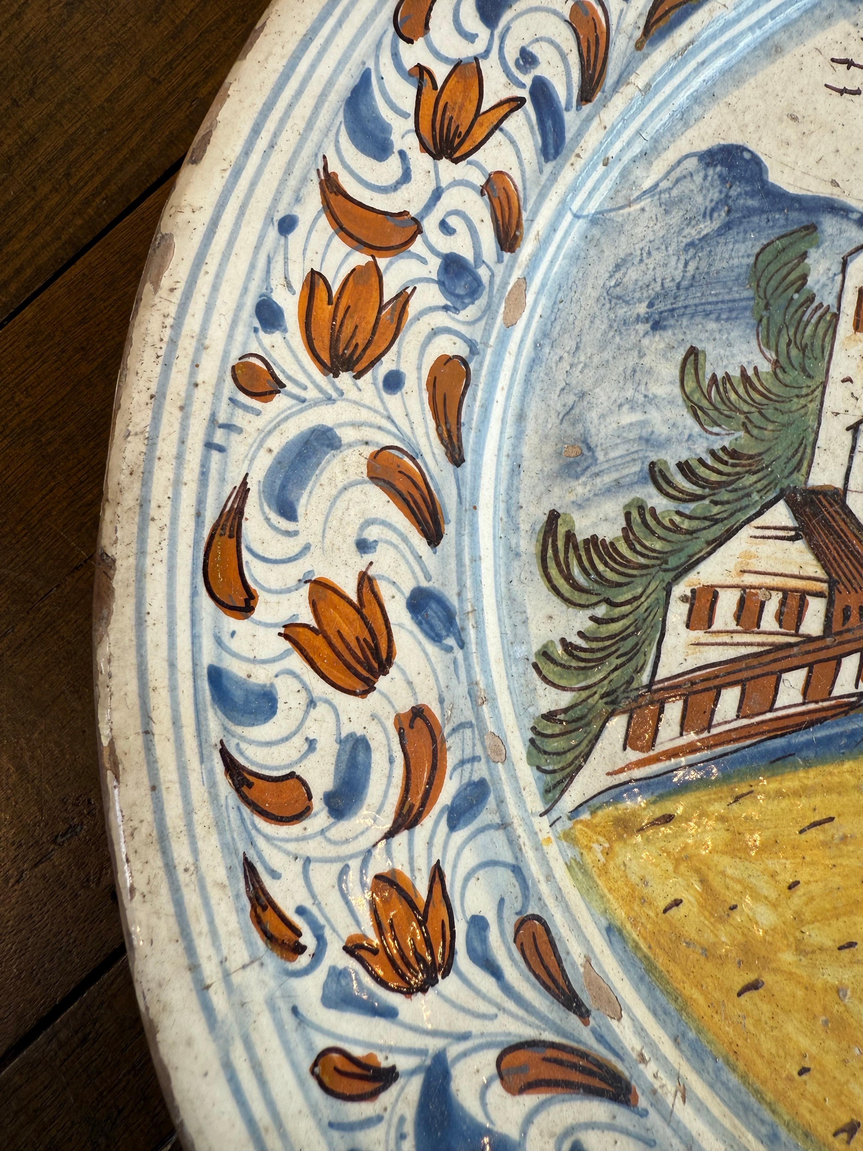 A Delft Polychrome Earthenware Plate, 18th Century
With scenic tondo bordered by floral marly.

Provenance: Private Australian Collection.

Dimensions:
Height: 4cm.
Diameter: 35.5cm.

Note:
This is a majolica plate, a type of tin-glazed earthenware