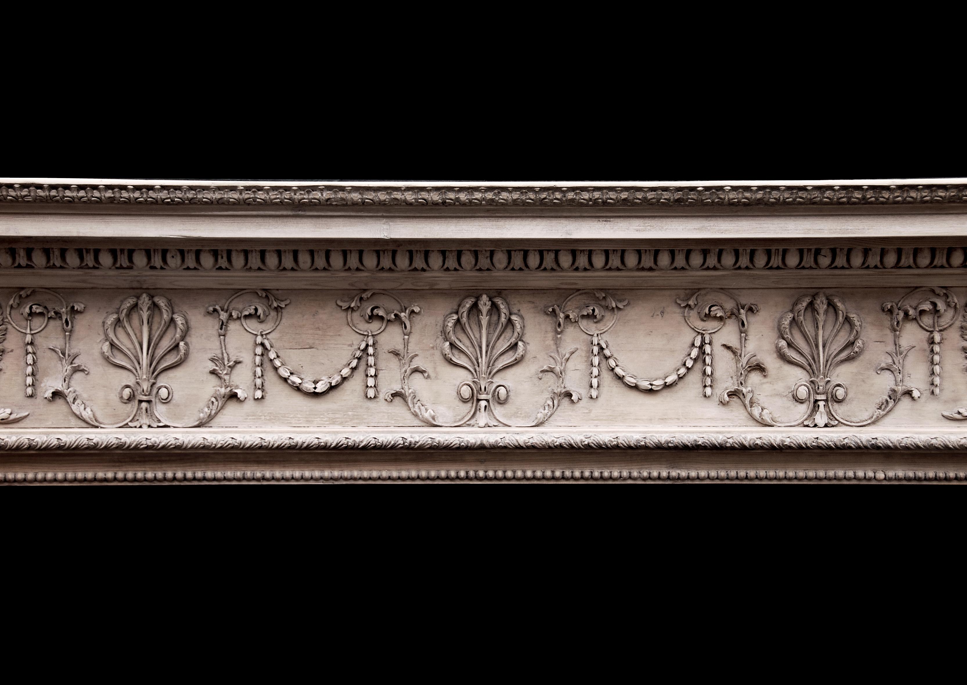 A delicate 18th century English pine fireplace. The carved frieze with honeysuckle, swags and foliage enrichments surmounted by egg-and-dart bed moulding and carved acanthus leaf shelf moulding. The jambs with carved oak leaf moulding and beading to