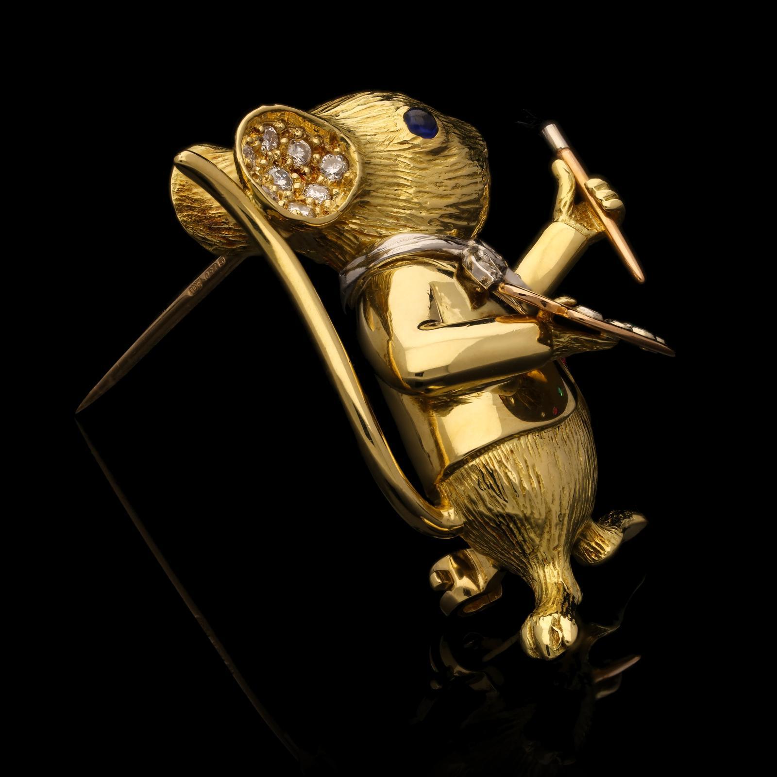 A delightful gold and gem-set mouse brooch 'Are you Manet or Mouse?!' by E. Wolfe & Co. 1990, the finely modelled three-dimensional standing mouse, anthropomorphised as an artist,  in 18ct yellow gold textured to resemble fur, wearing a gold jacket