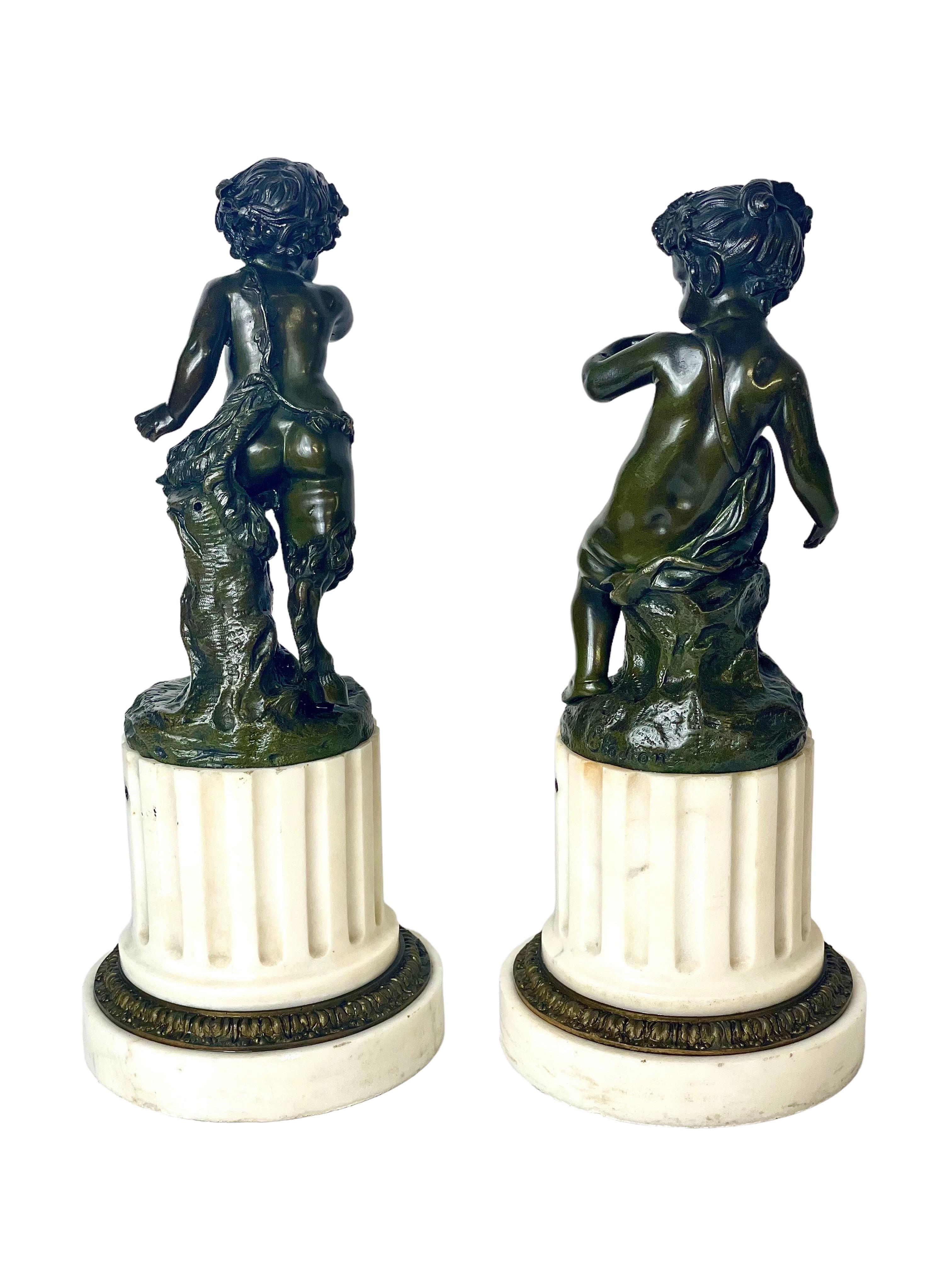 Ein reizvolles Paar patinierter Bronzestatuetten, ursprünglich Kandelaber, nach Clodion (Claude Michel Clodion 1738 - 1814), die einen jungen Satyr und eine Satyre darstellen. Sie sind auf stumpfen Säulen aus geriffeltem weißem Marmor montiert und