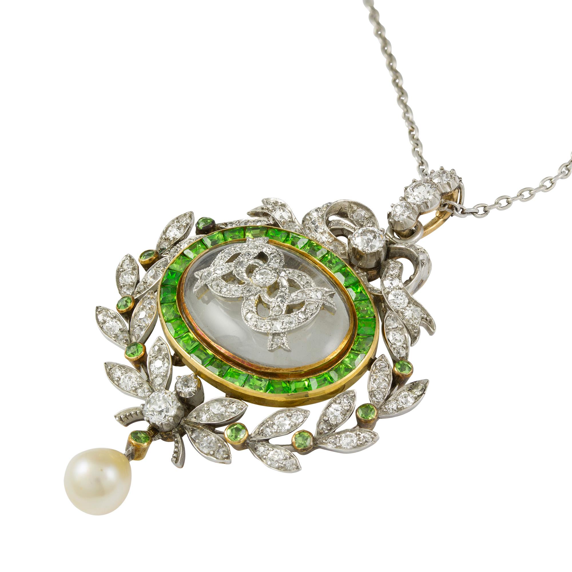 An Edwardian diamond and demantoid garnet-set pendant, to the centre an oval cabochon-cut rock crystal applied with diamond-set ribbon-like decorations, surrounded by twenty-eight calibre-cut demantoid garnets, within a diamond-set wreath flanked