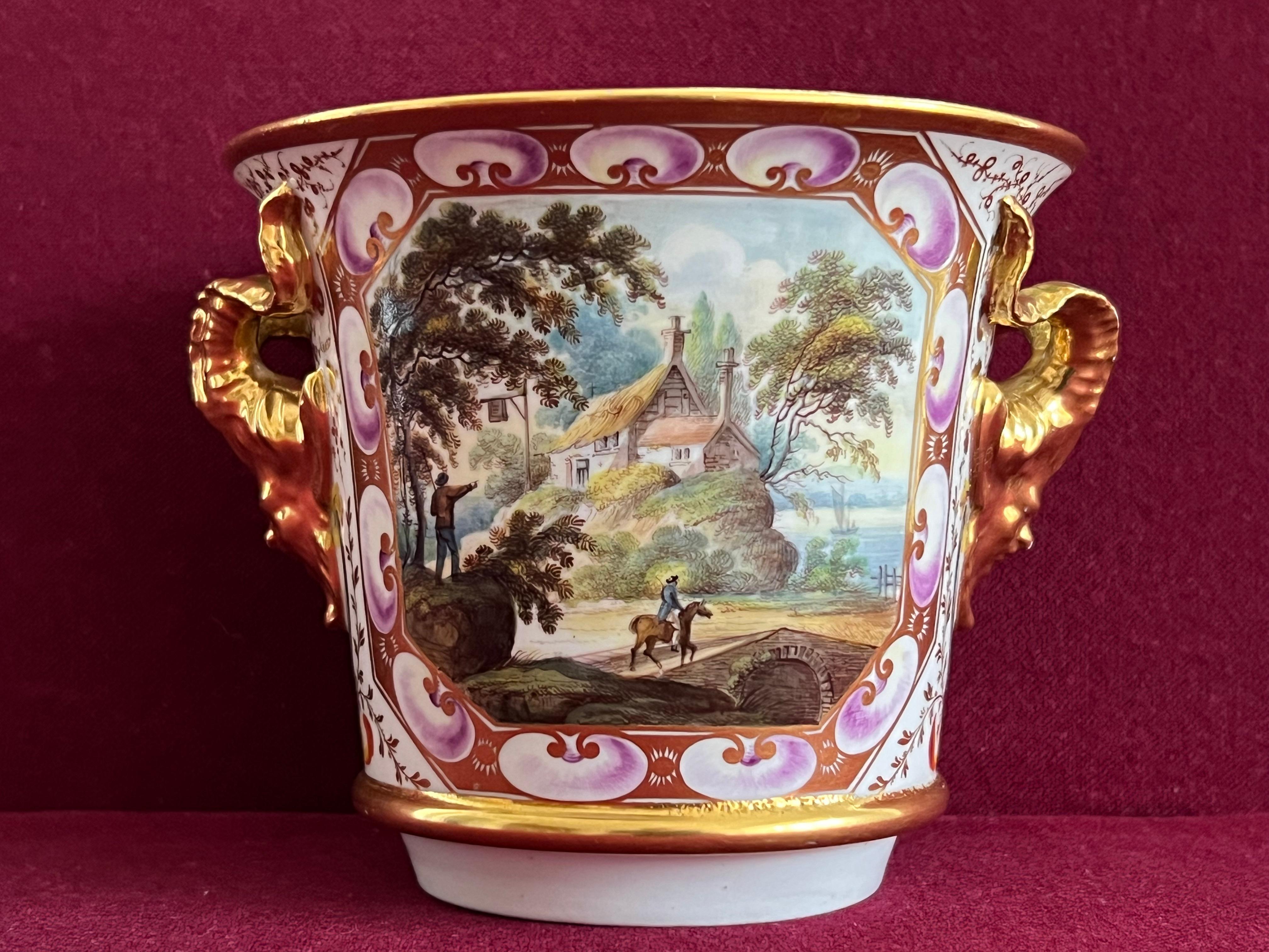 A Derby Porcelain Cache Pot c.1815. Of circular form, flared rim with slightly tapered sides, the front decorated with a finely painted by John Brewer with the scene of a man on horseback crossing a bridge and a Coaching Inn next to a river. 

Each