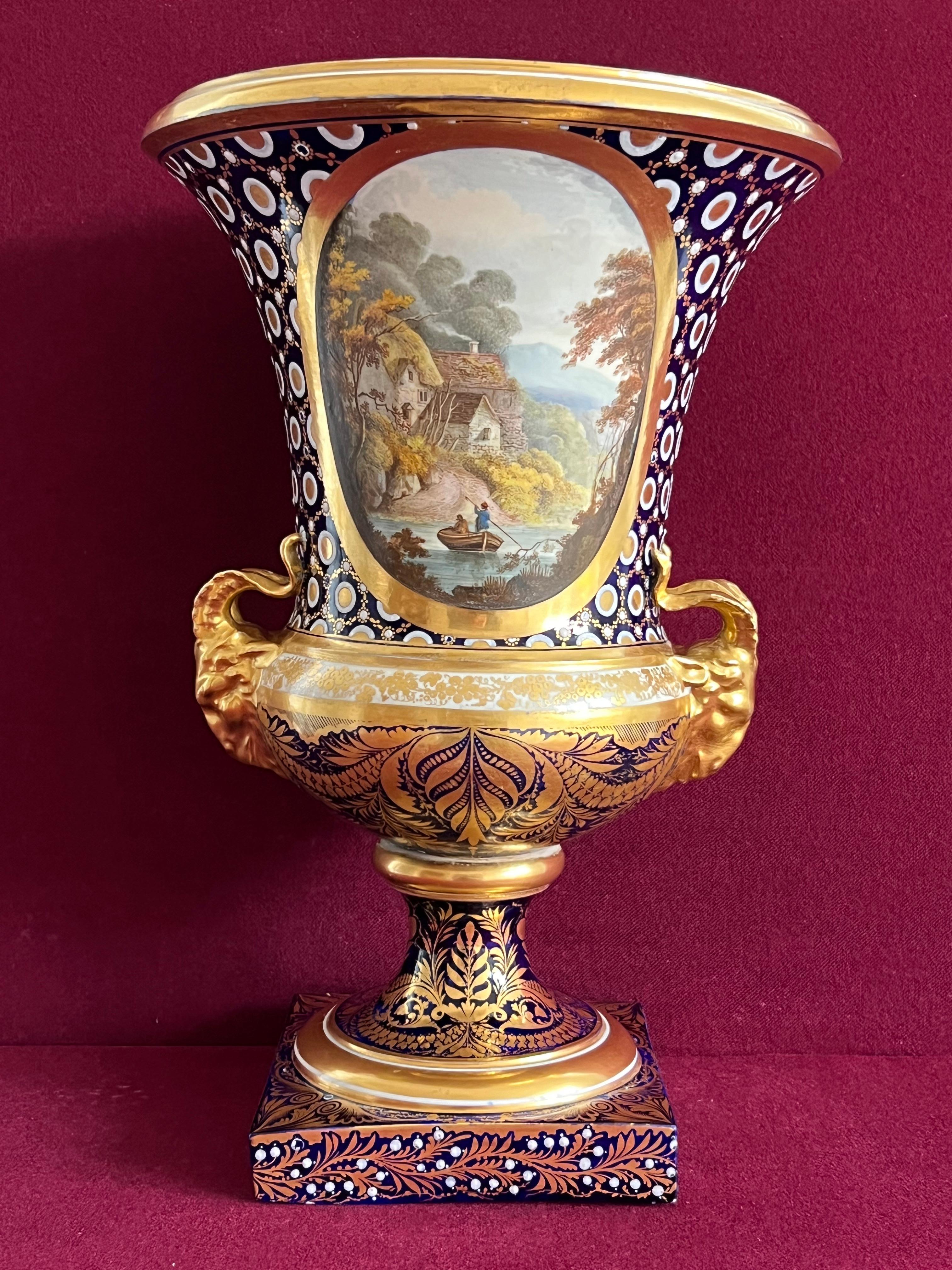 Grand vase Campana en porcelaine de Derby décoré par John Brewer vers 1810 - période Duesbury & Kean. Chaque côté du vase est finement peint d'un rondeau, l'un avec un paysage marin et l'autre avec une scène de rivière et une chaumière, avec des