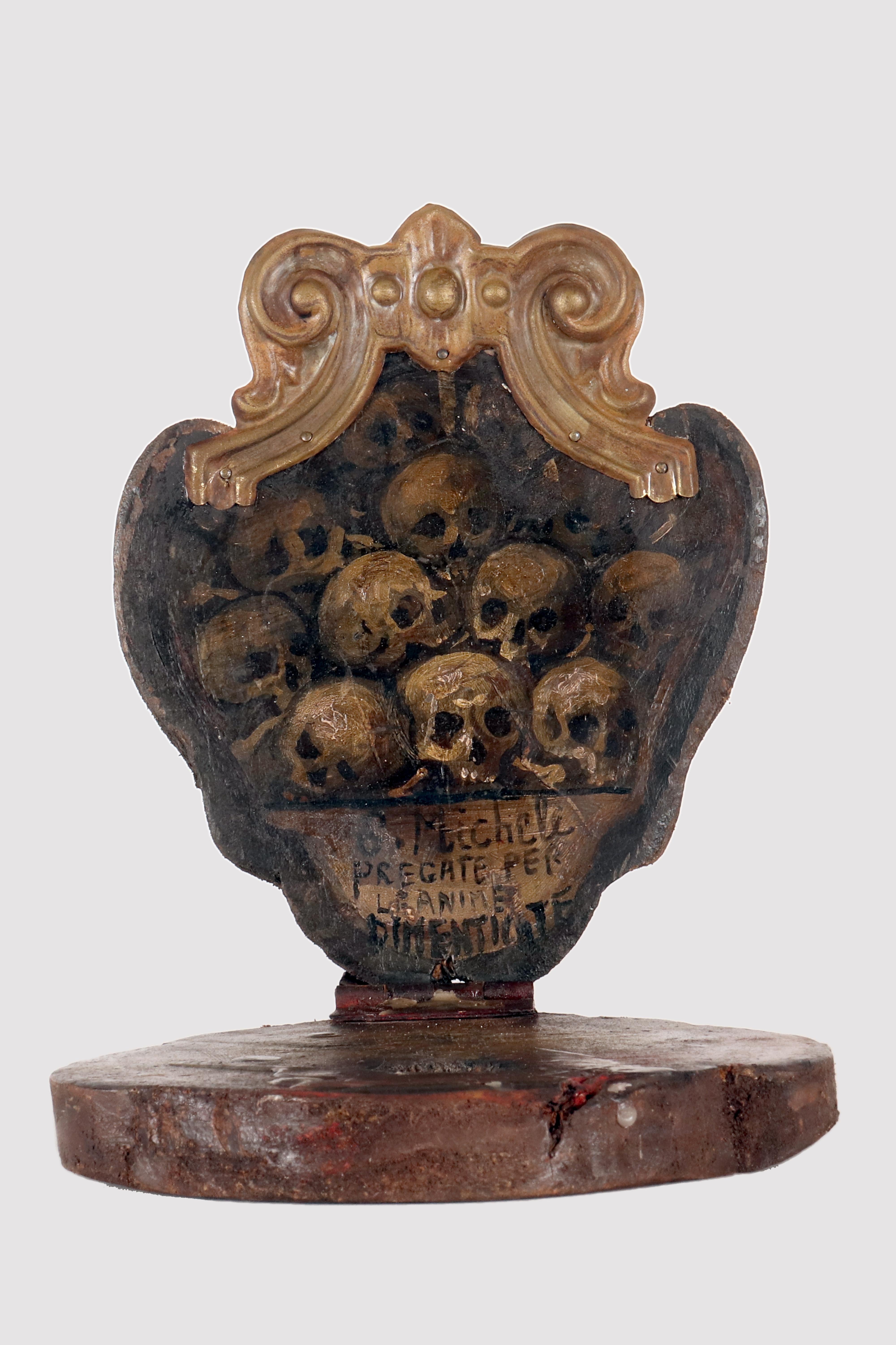 Un sanctuaire de dévotion, un Memento Mori, fabriqué en bois de fruitier avec deux panneaux juxtaposés articulés à la base, et couronné d'une flamme en métal. Le dos comporte un trou pour le clou utilisé pour l'accrocher au mur pendant le service de